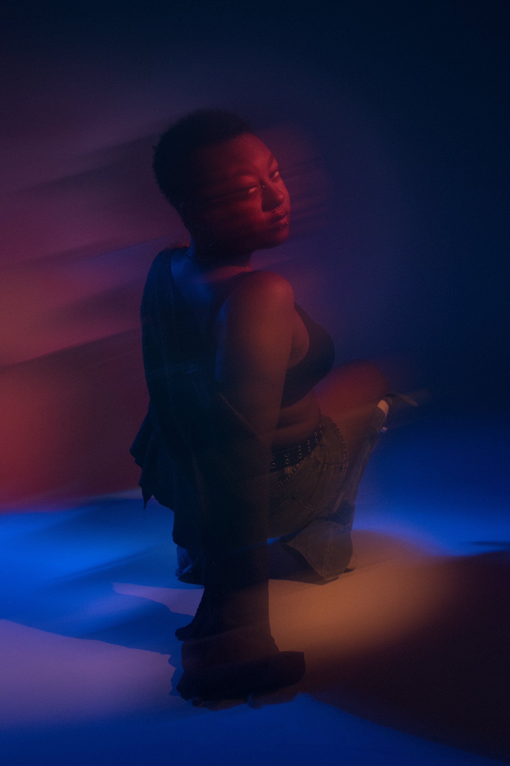 Person kneeling with head bowed, eyes closed, amidst colorful, soft lighting with shades of blue, red, and purple.