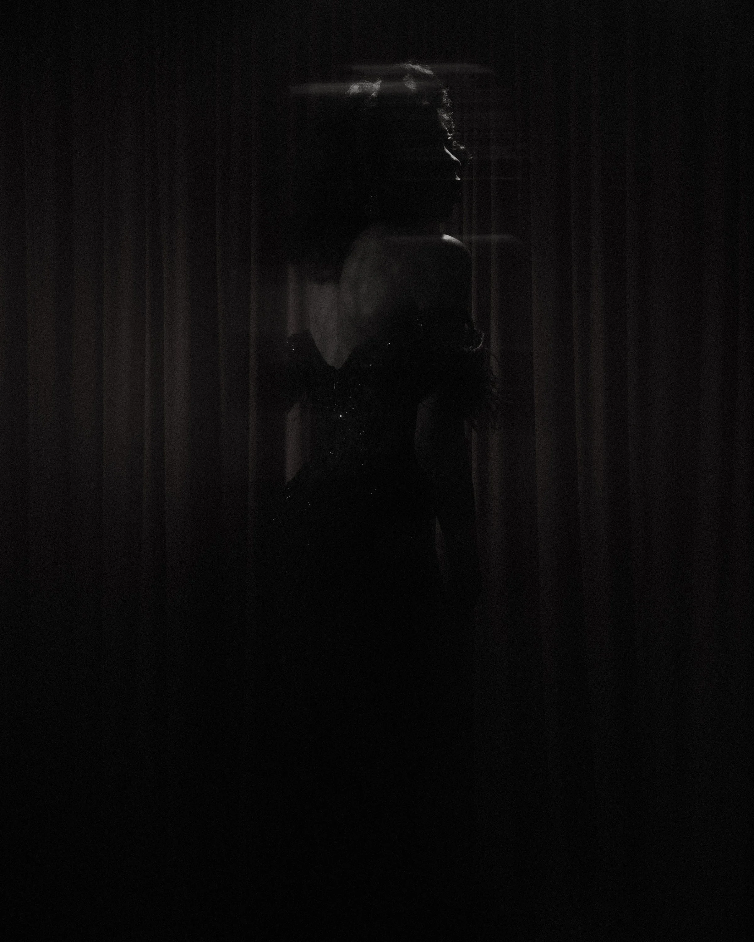 Dark image with a silhouette of a woman in a dress, viewed from the side, with minimal lighting highlighting her face and face outline