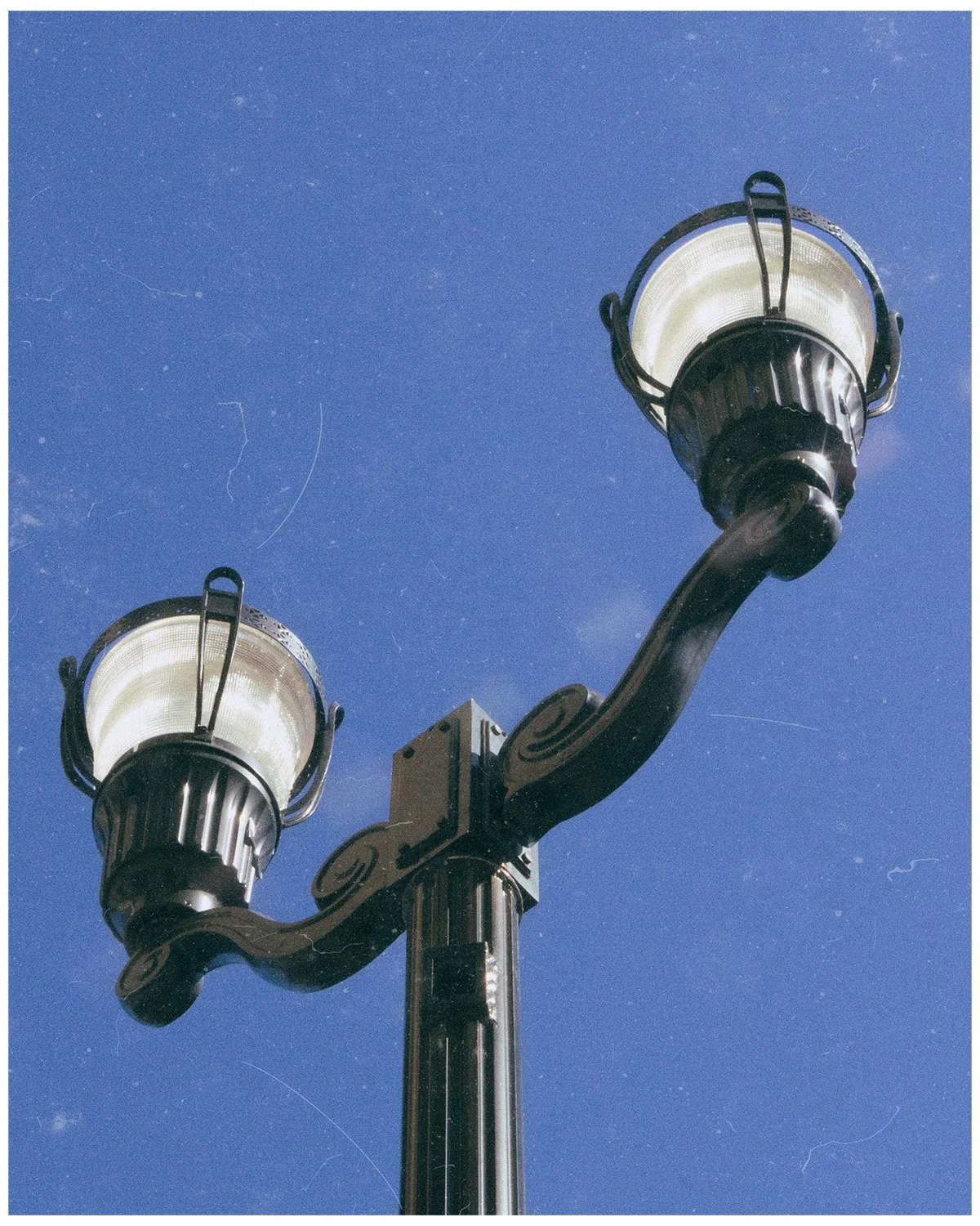 A black metal street lantern with two lights against a clear blue sky.