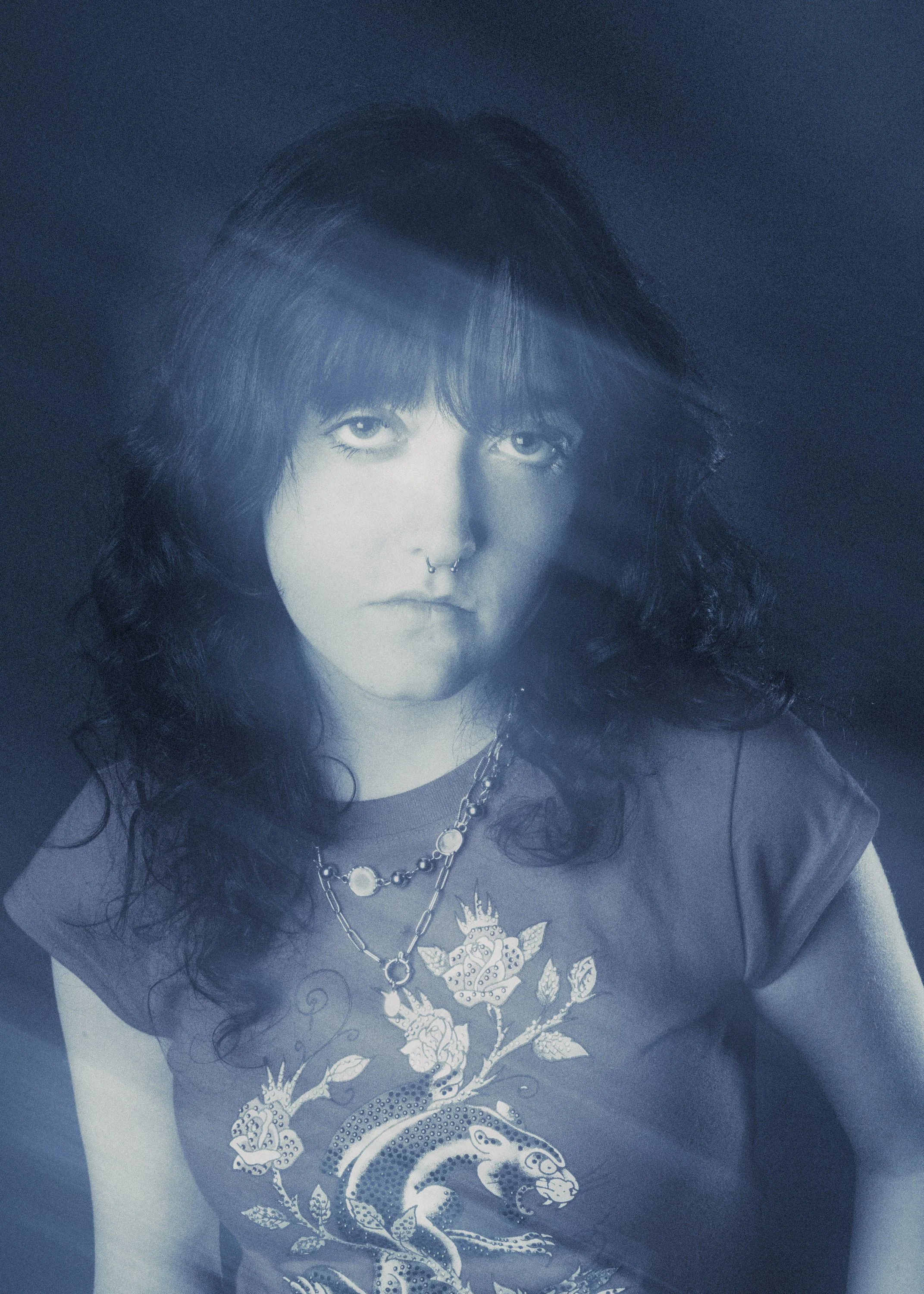 A woman with long curly hair wearing a jewelry chain and a T-shirt with a dragon design.