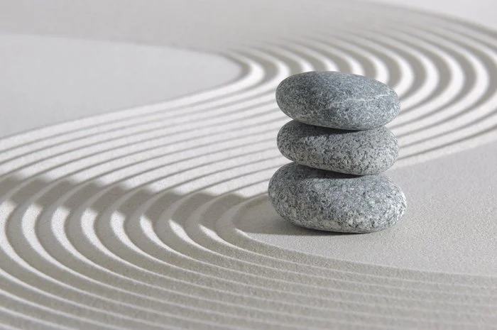 Three stacked gray stones on a zen garden with raked sand and curved lines.