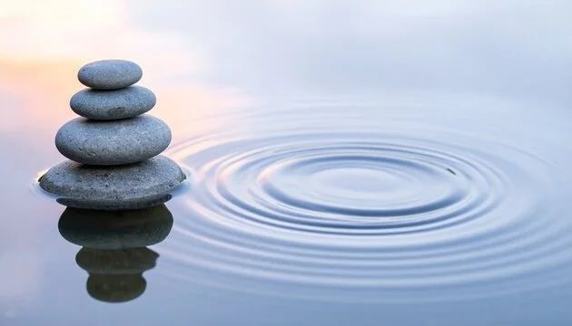Stacked smooth gray stones on water surface with ripples nearby