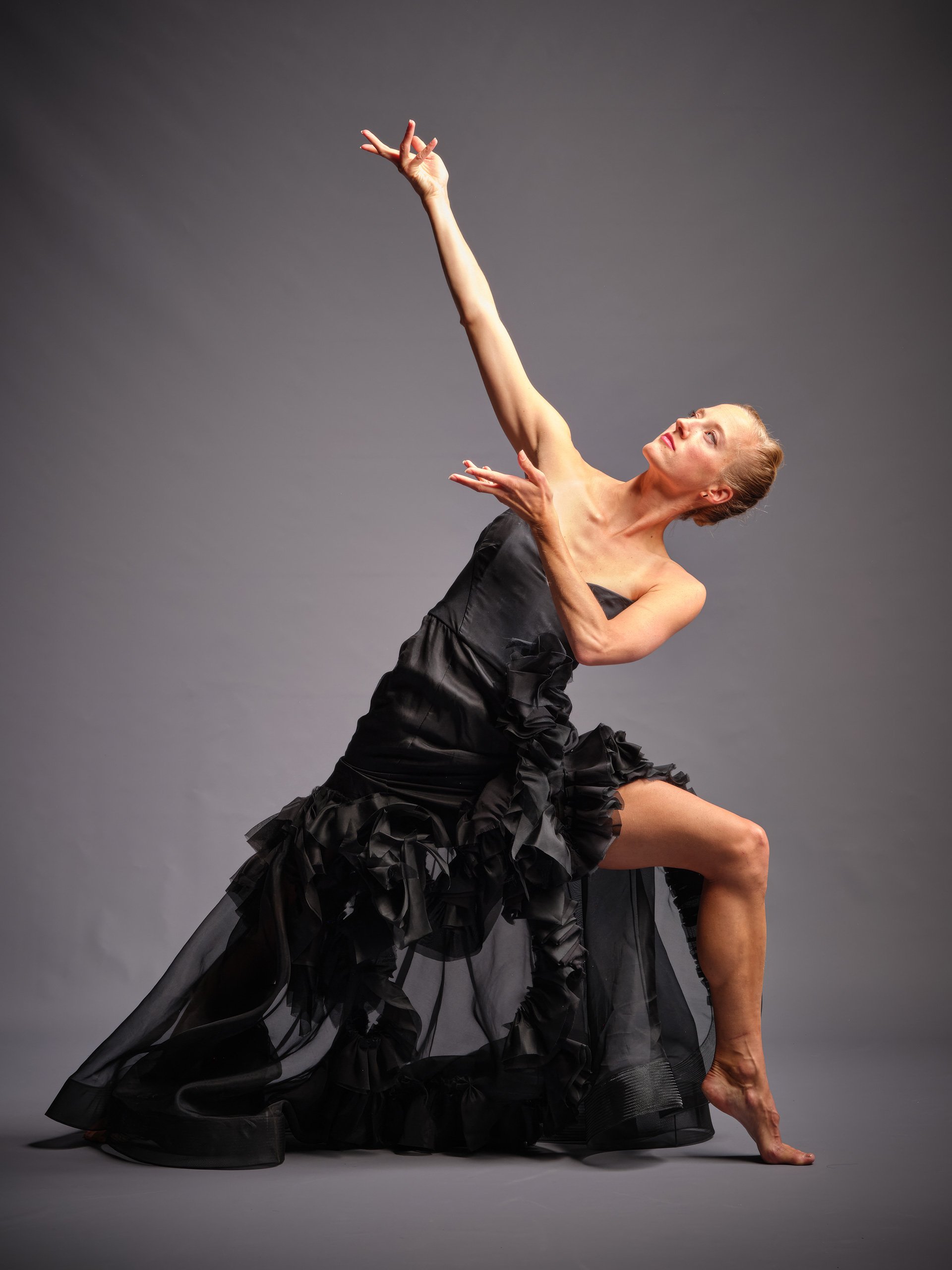 Michaela Ellingson in a dance pose with hand titled high on a gray background.