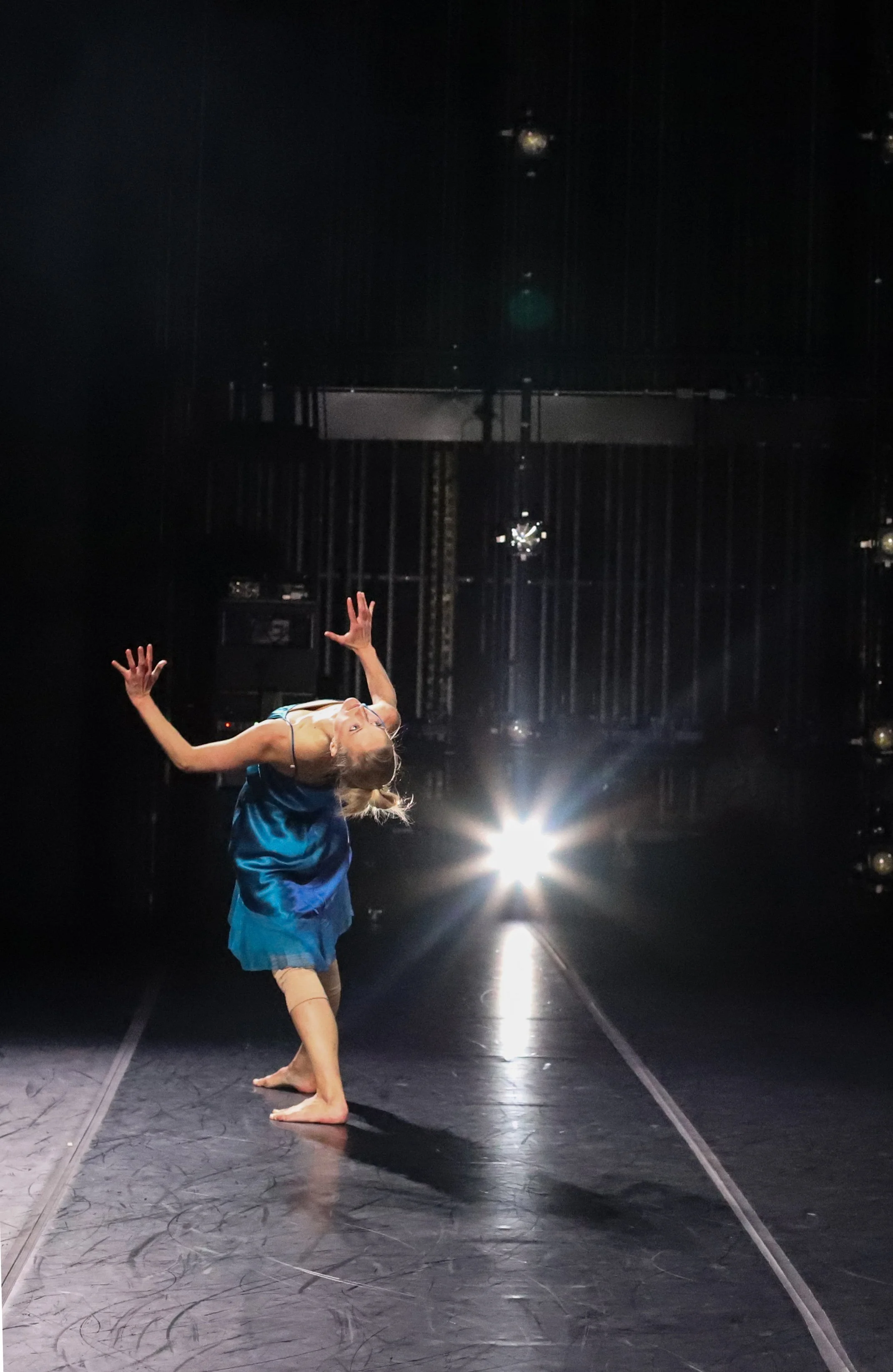 Michaela Ellingson in a blue dance costume performing a dance move on a stage with a dark background and bright lights.