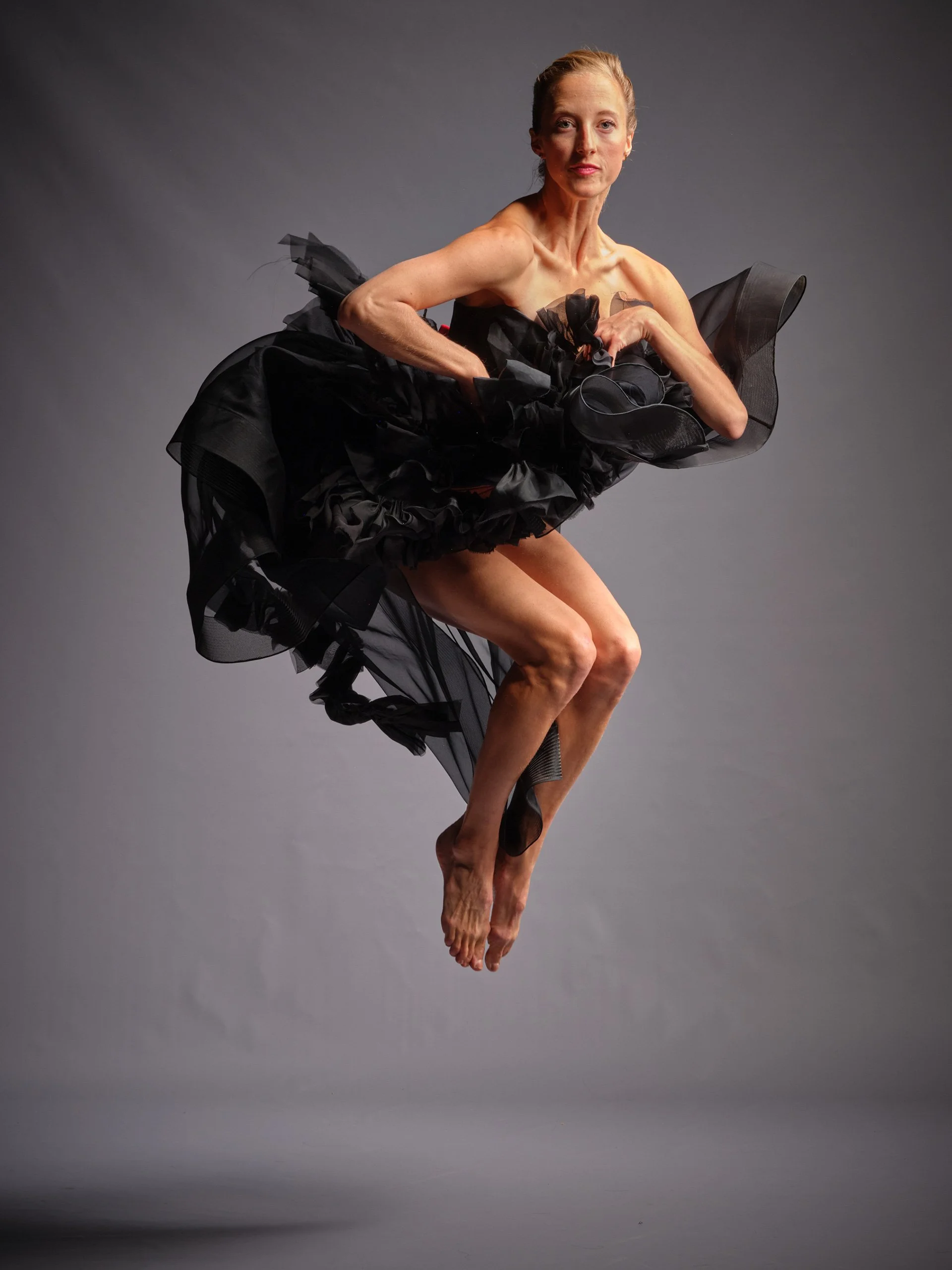 Michaela Ellingson in a dance pose jumping off the ground, with toes pointed downward with a black flowy dress on.