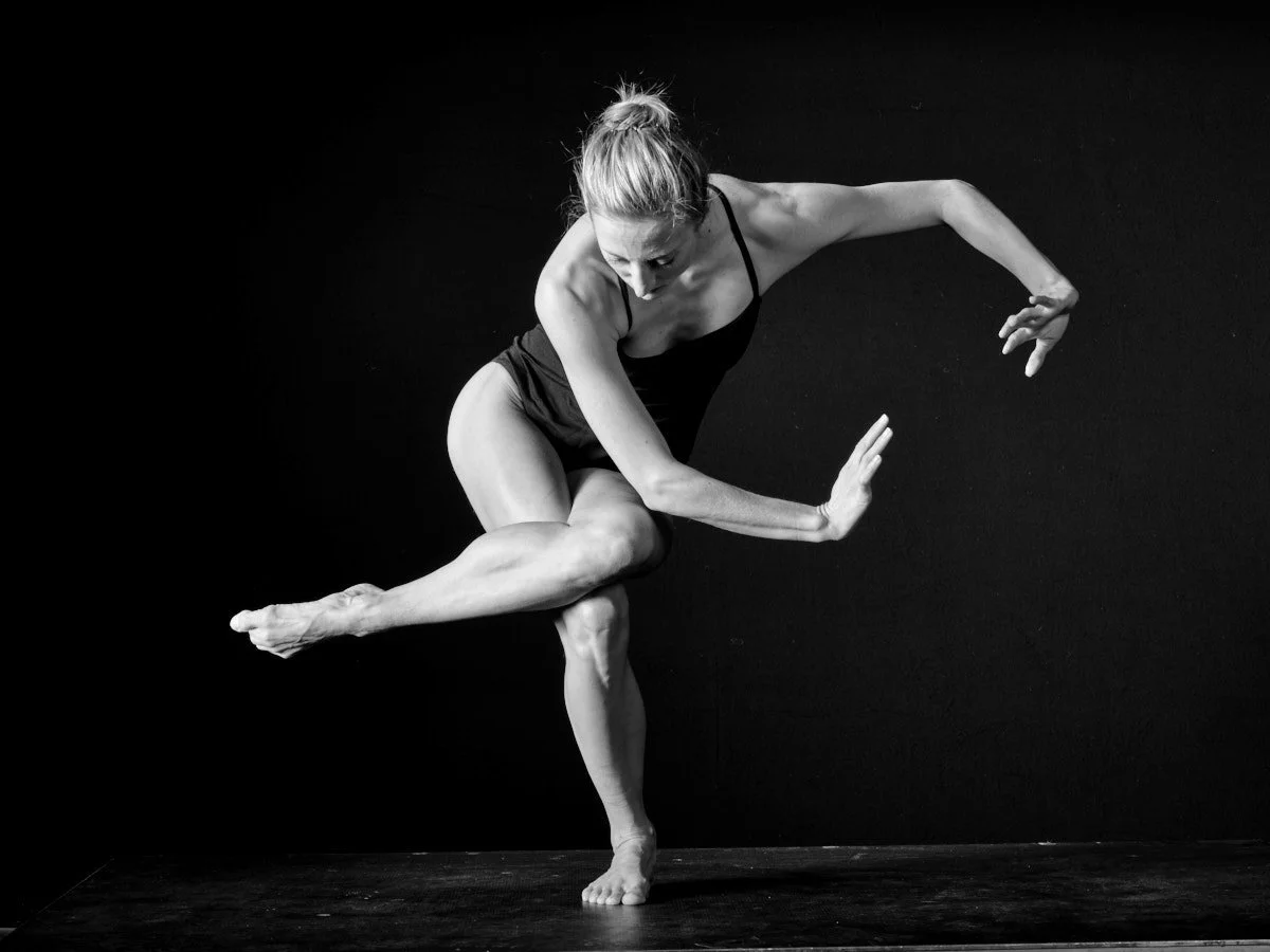 Michaela Ellingson performing a dance or gymnastics move against a black background, balancing on one foot with her other leg extended and arms positioned for balance.