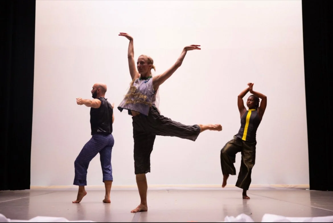 Three dancers performing on stage with a plain white background, each in different poses.