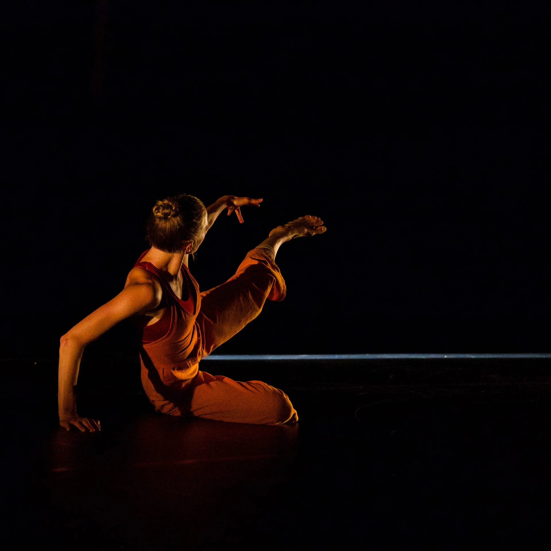 Person performing a yoga pose in a dark setting, with only their face, arms, and part of their body illuminated.