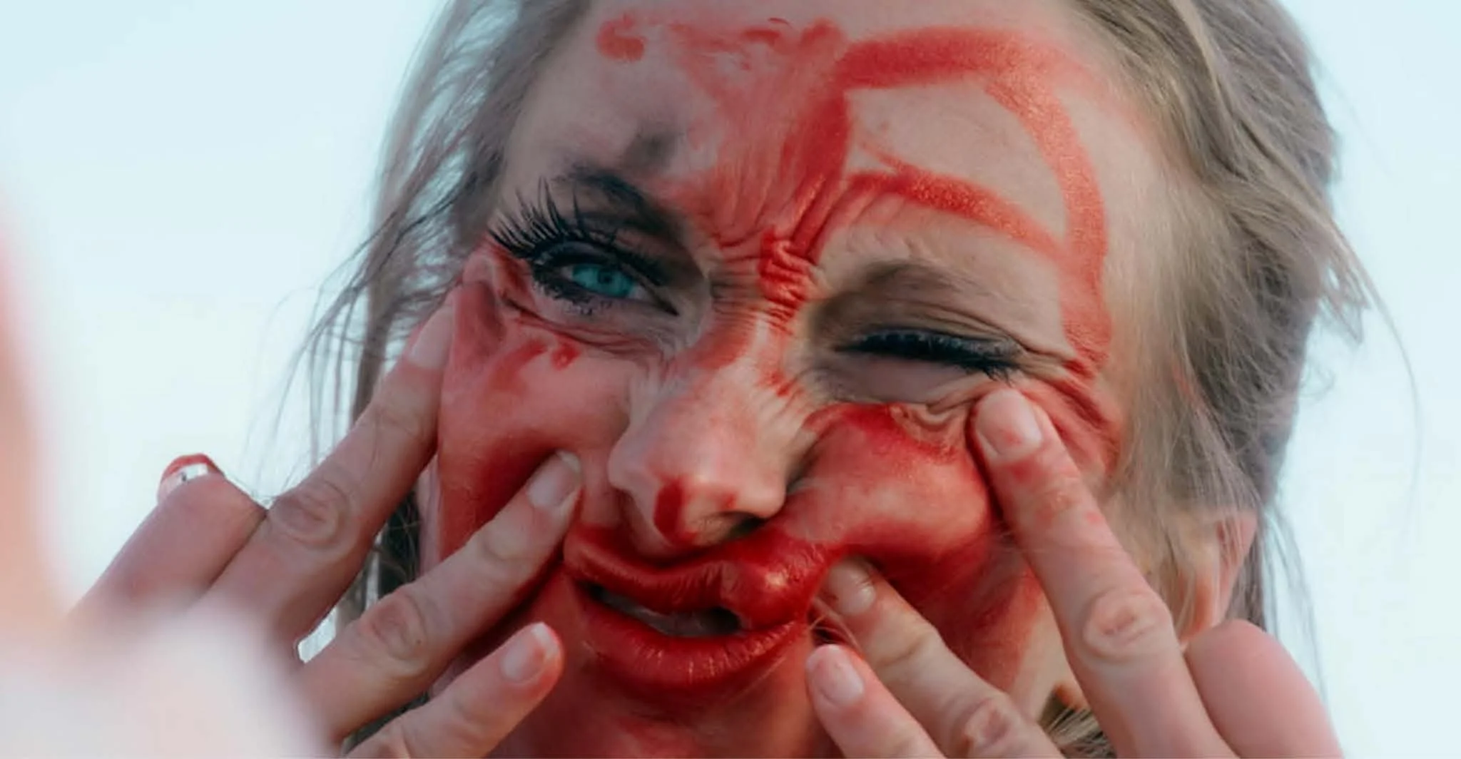 Michaela Ellingson with face covered in red paint or makeup, smiling and making a playful gesture with her fingers around her eyes.
