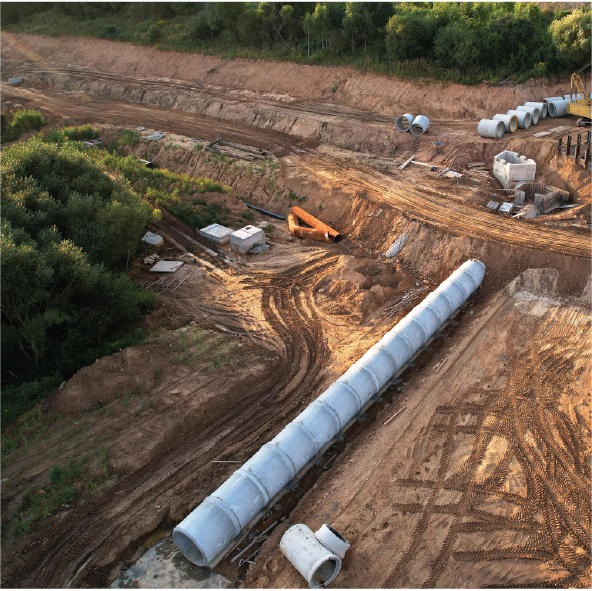 A construction site with large concrete pipes, construction equipment, and cleared land for a pipeline installation.