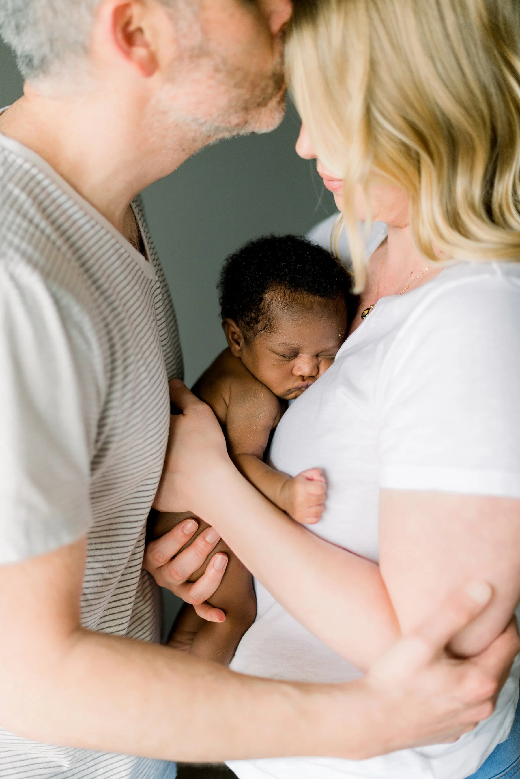 A couple holding a newborn baby close to their chests, with their foreheads touching, in a tender moment of care and love.