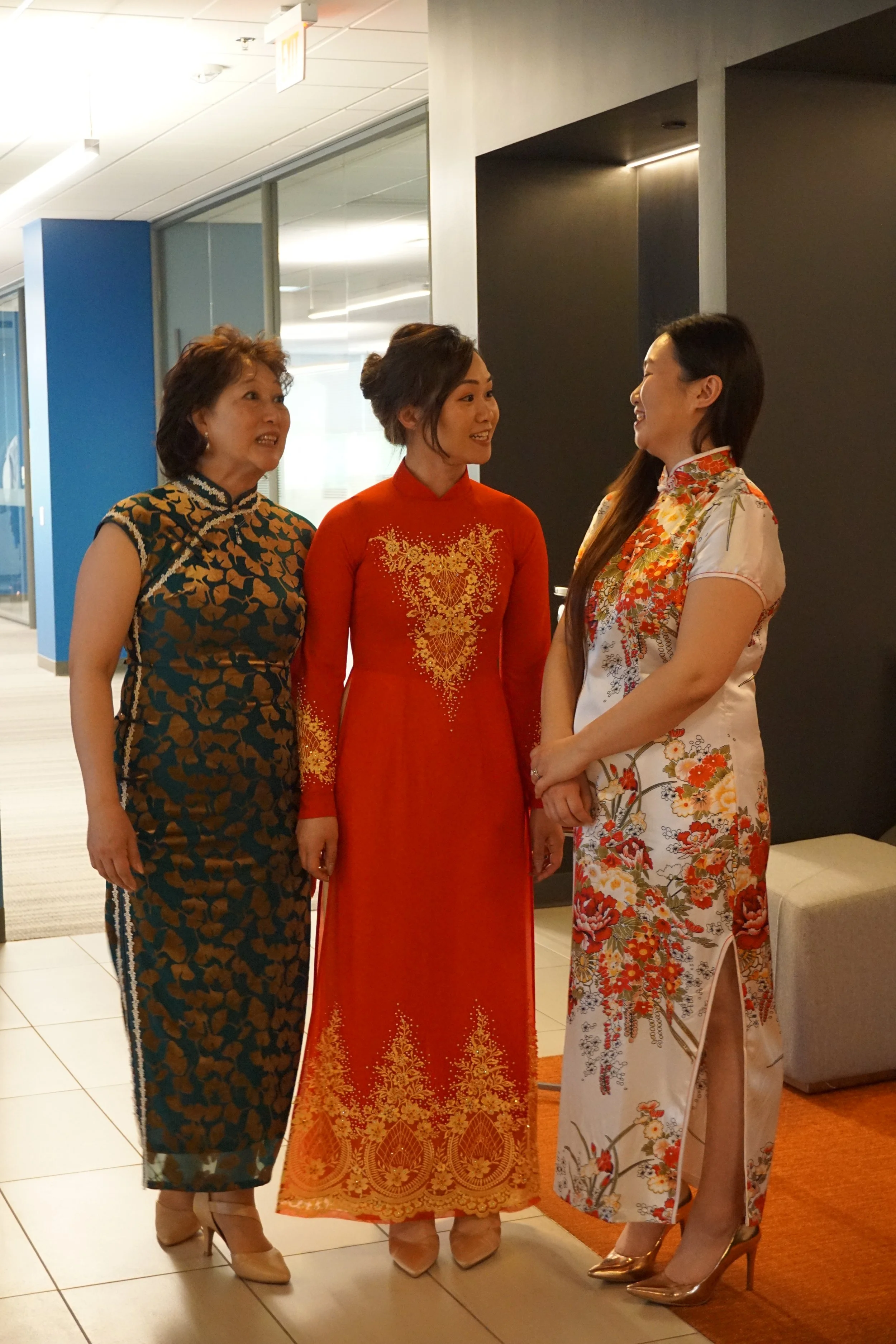Three women dressed in traditional Chinese cheongsams standing and talking in an indoor setting.