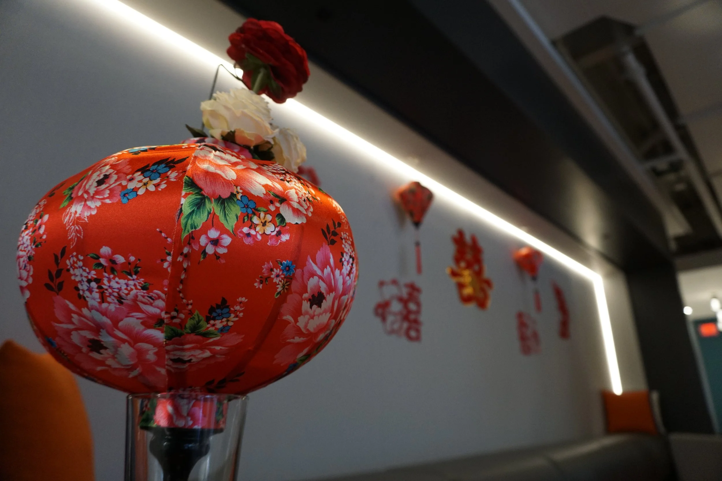Close-up of a red and floral Chinese lantern on a glass holder, with white and red flowers on the wall in the background