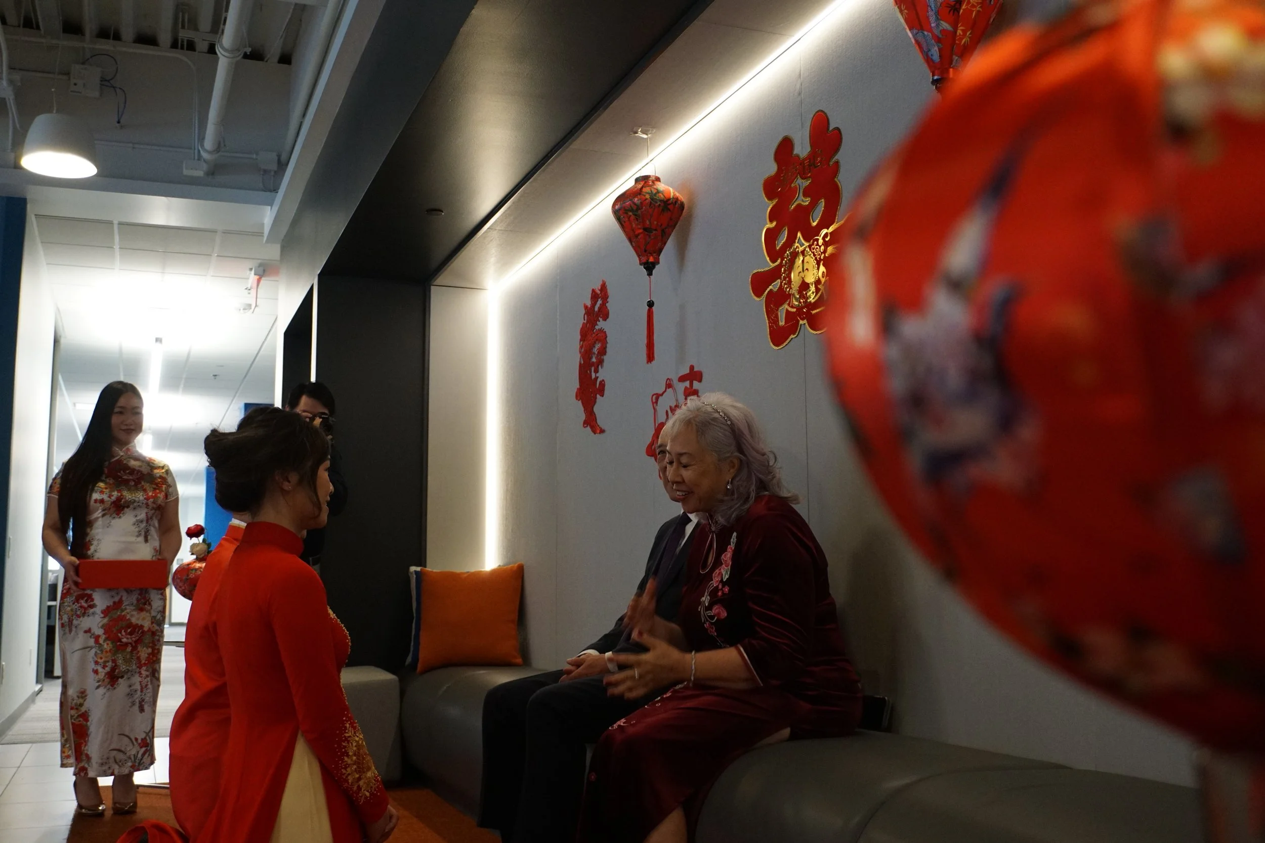 Celebration with Asian women dressed in traditional clothing, sitting and standing in a room decorated with Chinese symbols and lanterns.