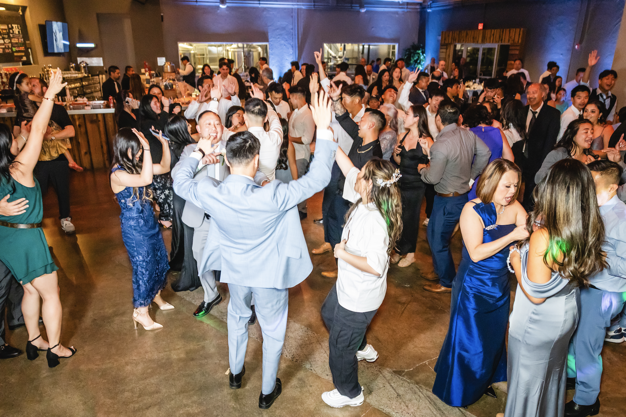 Crowd of people dancing and celebrating at a party or wedding reception in a decorated venue.