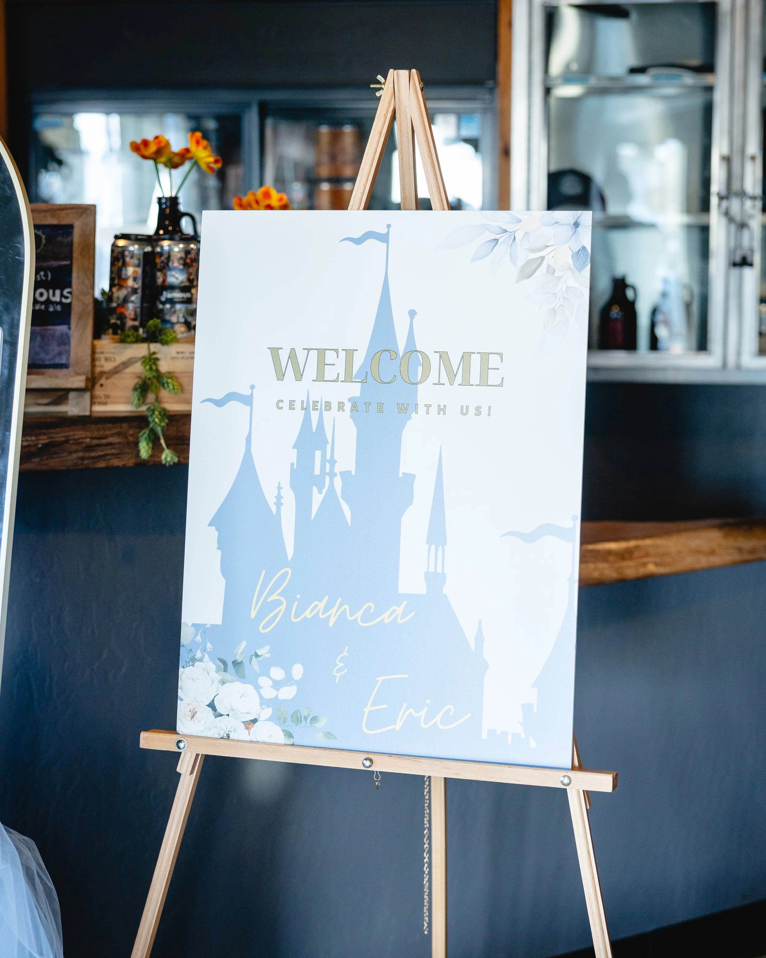 Wedding welcome sign with castle graphic, reading 'Welcome, Celebrate with us! Bianca & Eric', on an easel in a decorated setting.