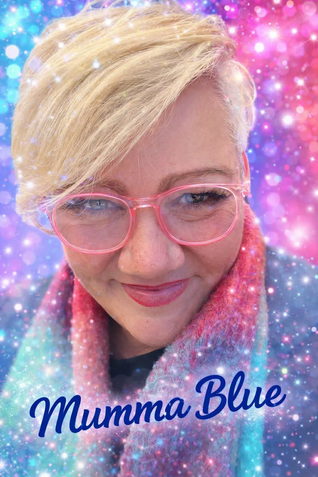A woman with short blonde hair wearing pink glasses and a colorful scarf, smiling with a sparkly, colorful background. The text 'Mumma Blue' is written at the bottom.