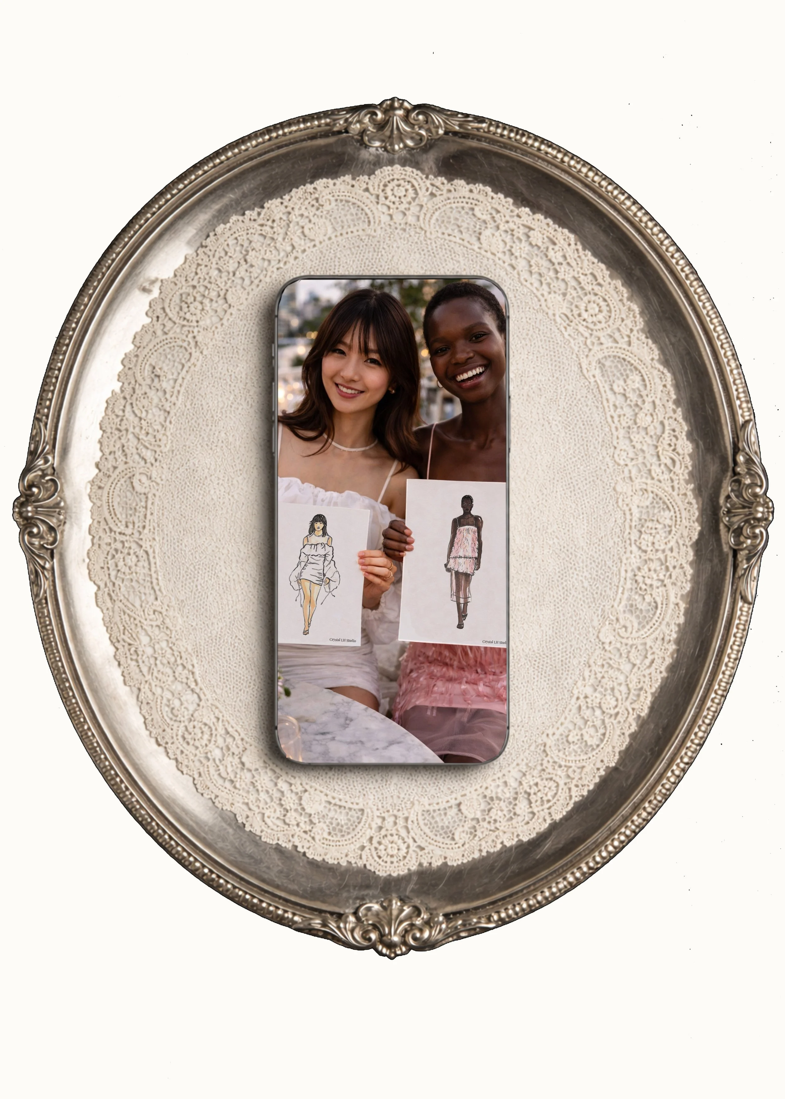 Two women smiling and holding fashion sketches, displayed on a smartphone, placed on a decorative silver tray with intricate lace-like pattern.