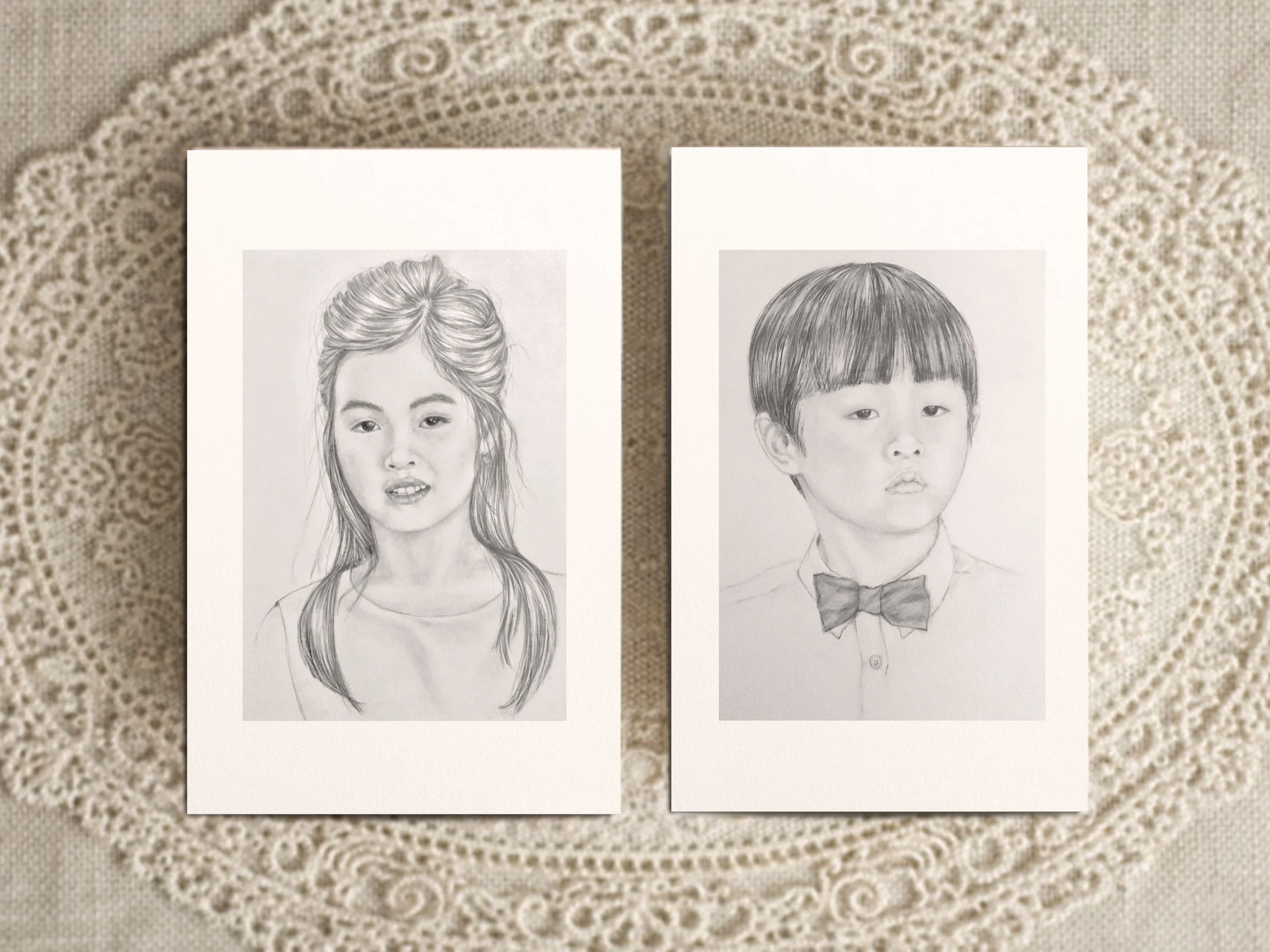 Two hand-drawn pencil portrait commissions of children displayed on white art cards.