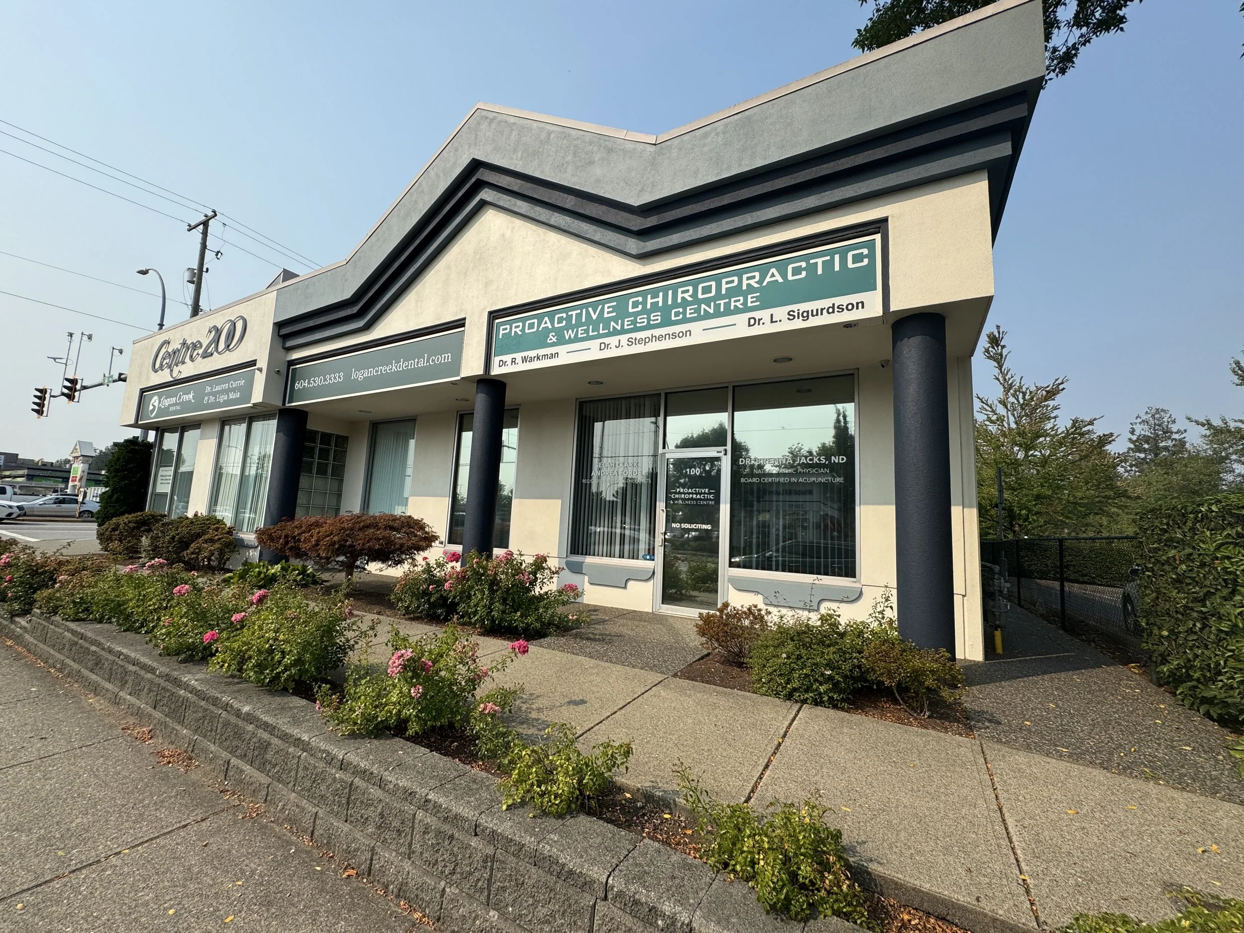 Exterior view of a office location at Proactive Chiropractic & Wellness Centre and a landscaped sidewalk with flowering plants and bushes.