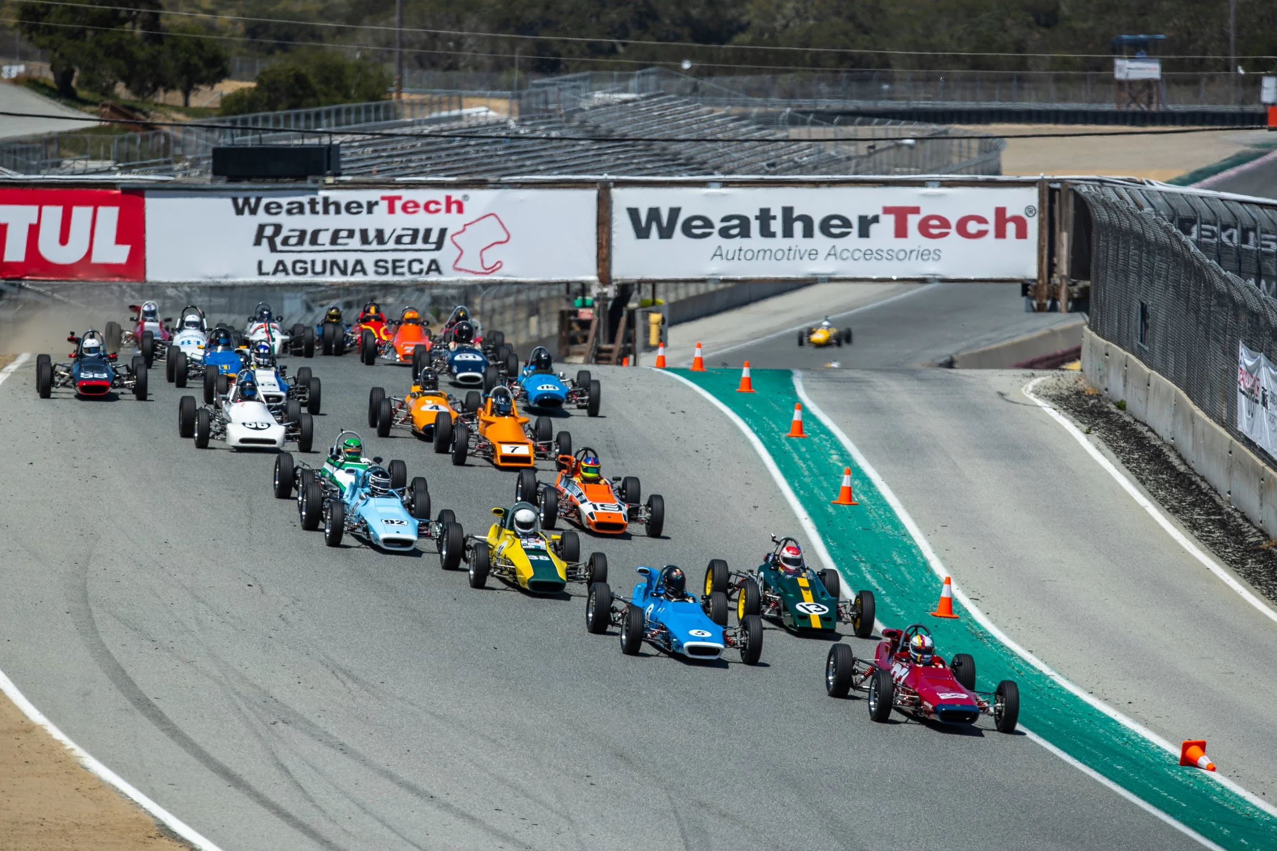 Race cars on a race track heading into a turn at Laguna Seca Raceway during a race event.
