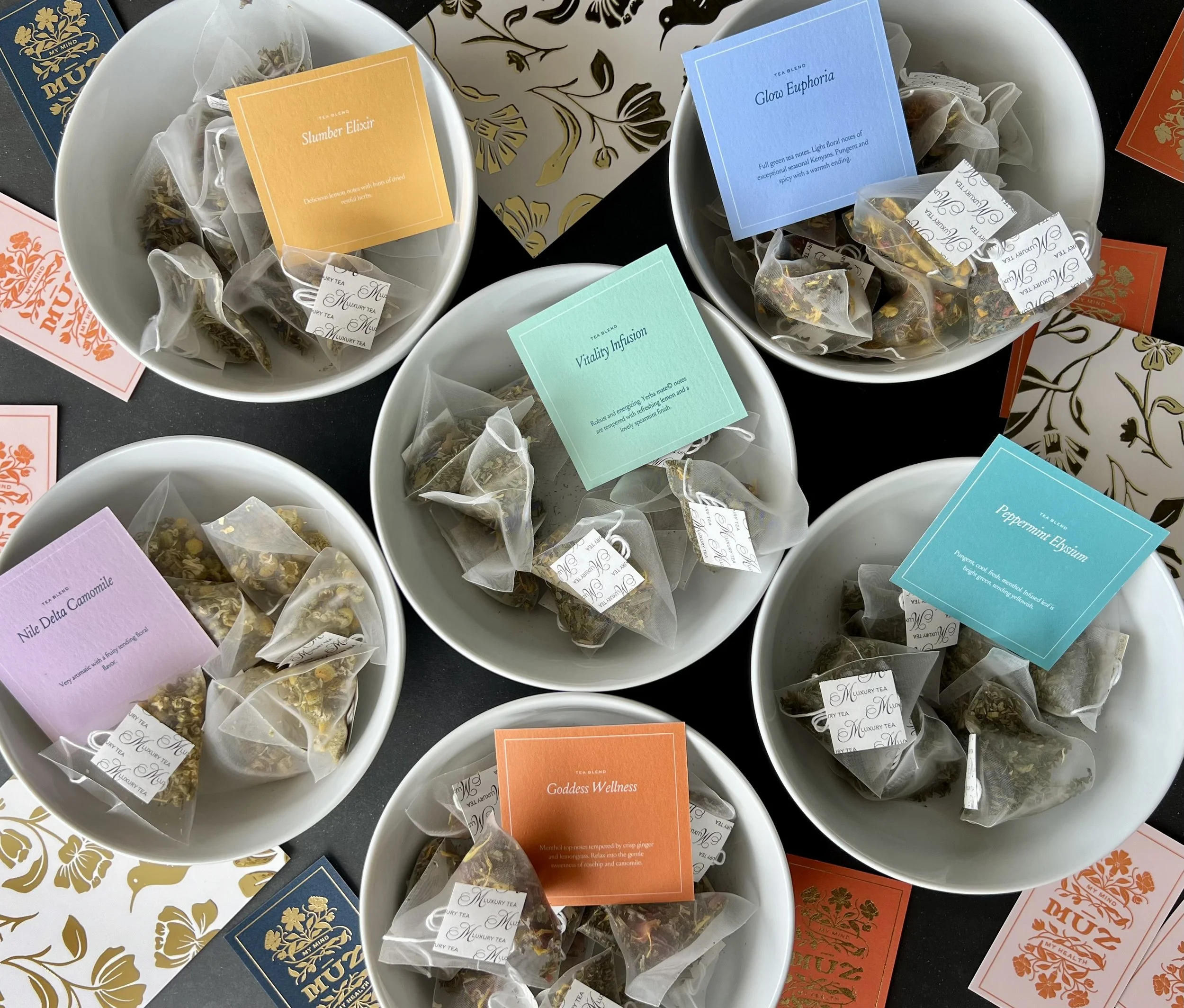 MŪZ luxury tea blends including Slumber Elixir, Glow Euphoria, and Vitality Infusion displayed in bowls.