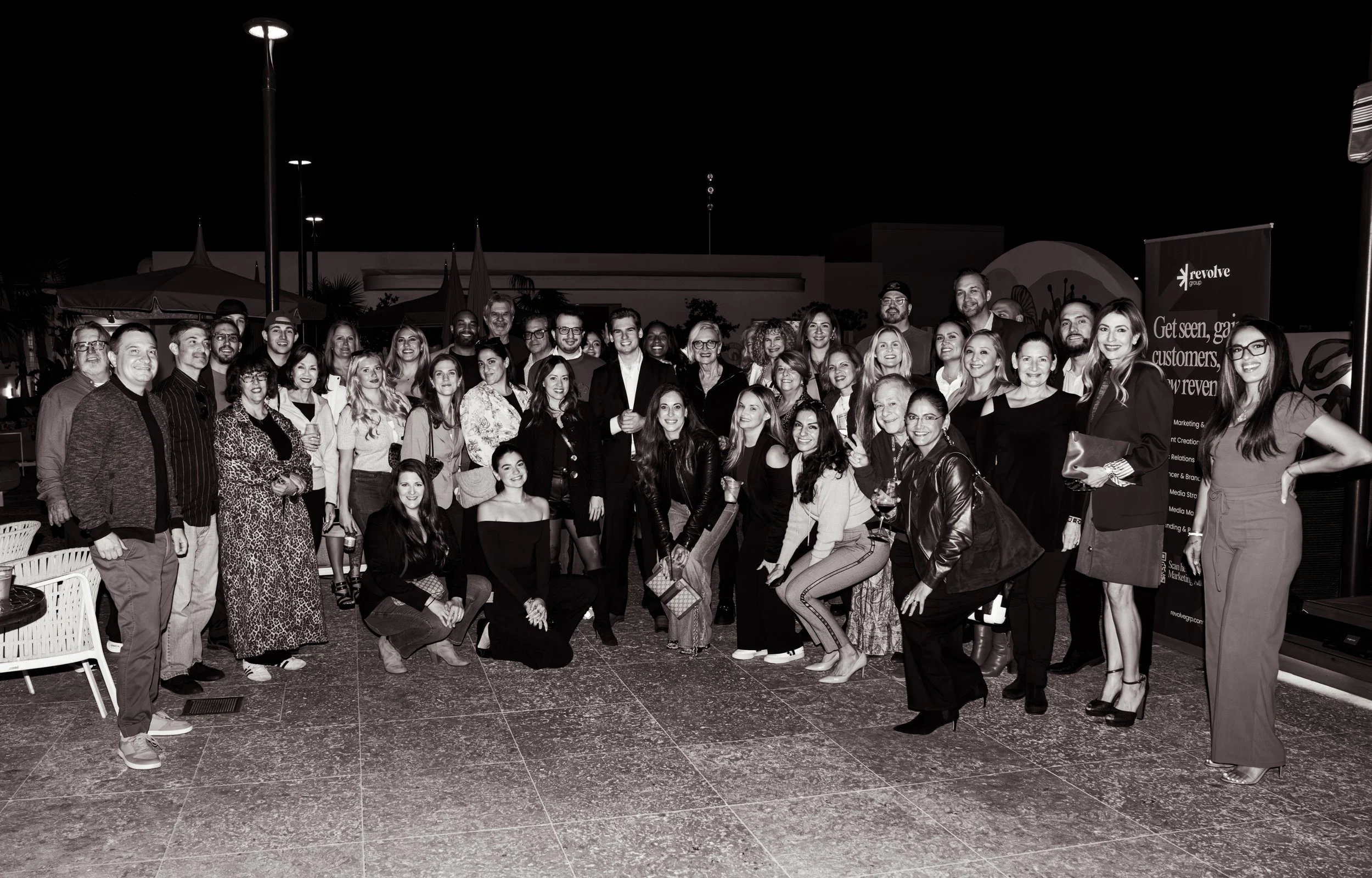 A large group of people smiling and posing together at an outdoor event during nighttime.