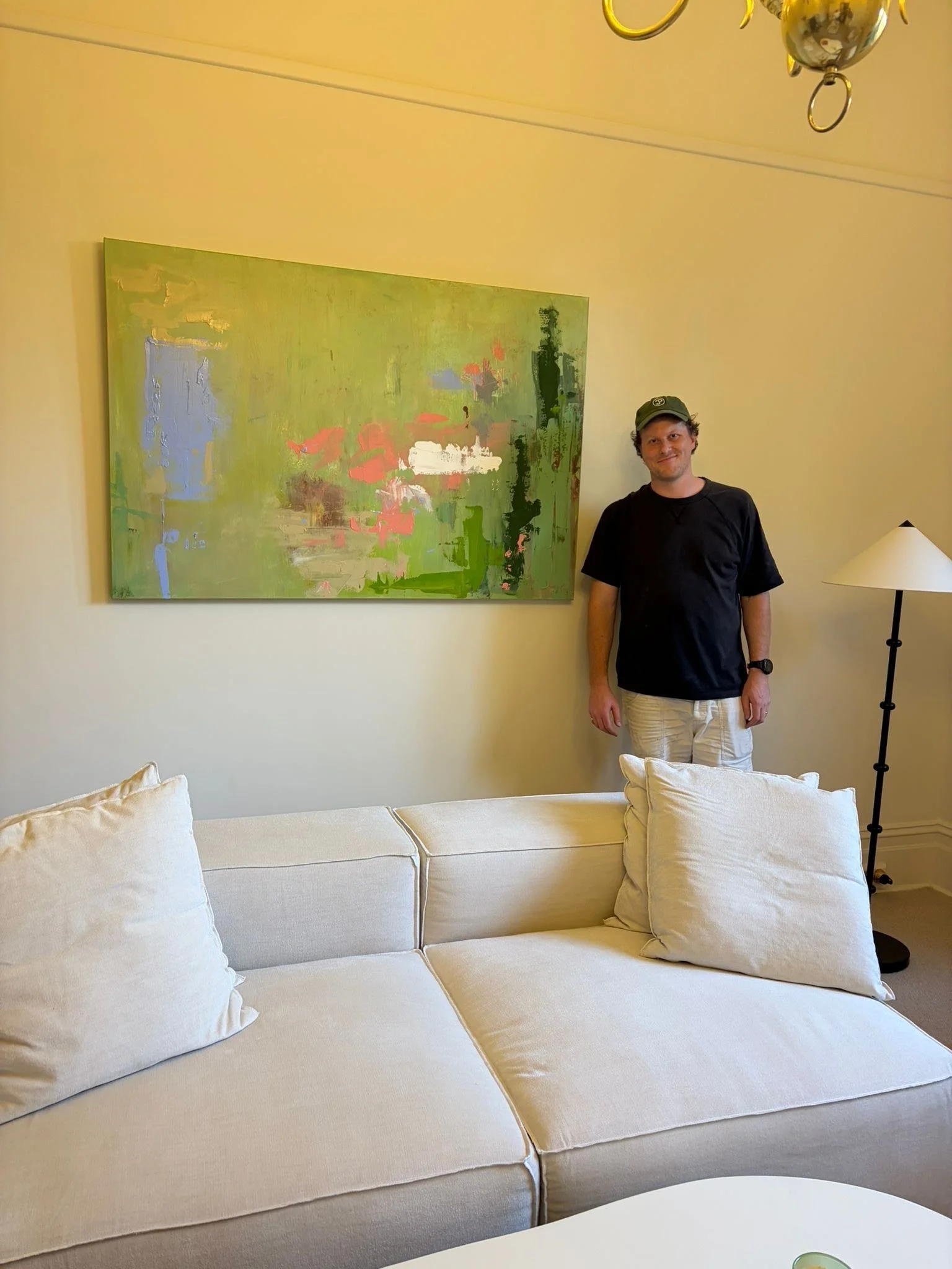 Thomas Cain standing beside his commissioned painting R, a large green abstract hanging above a cream sofa, 150 x 100 cm