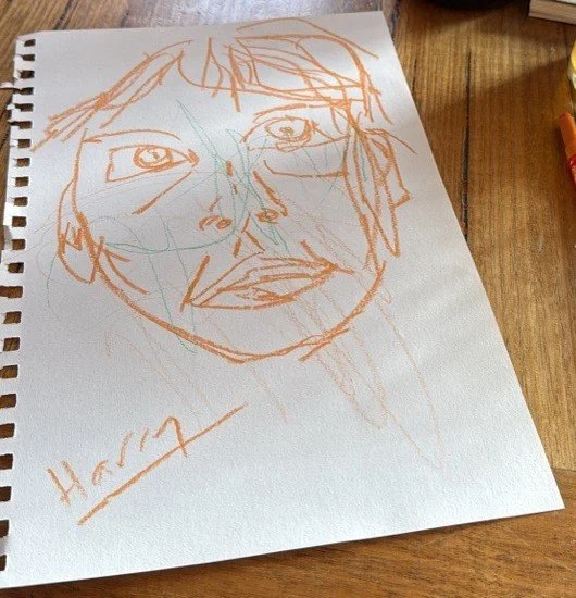 An orange crayon face drawing made at the pub, where Thomas Cain started drawing in 2025