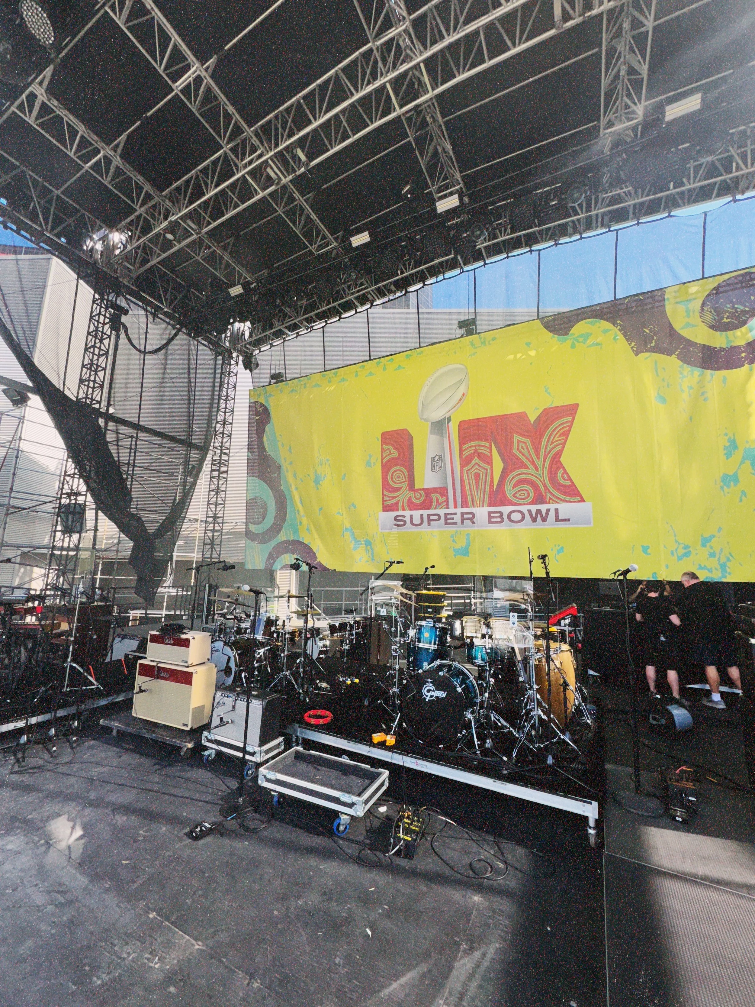 Stage setup with musical instruments and equipment, with a large yellow Super Bowl LIV banner hanging overhead.