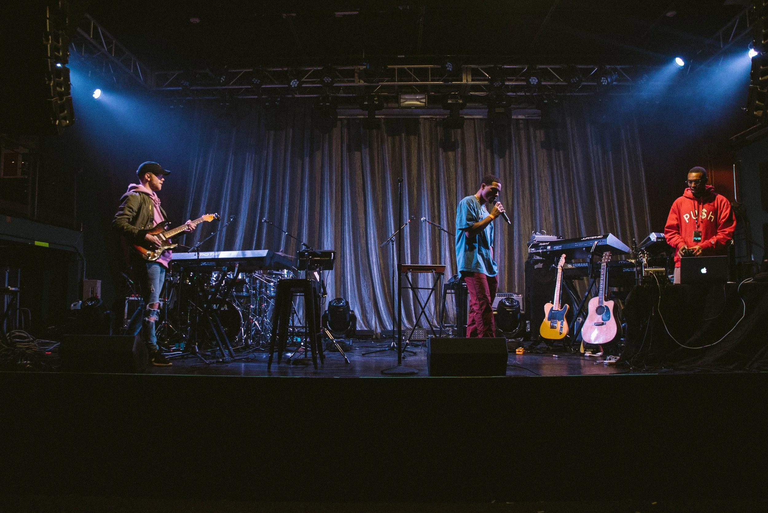 Three musicians on a stage with musical instruments, stage lights, and a curtain backdrop, preparing for a performance.