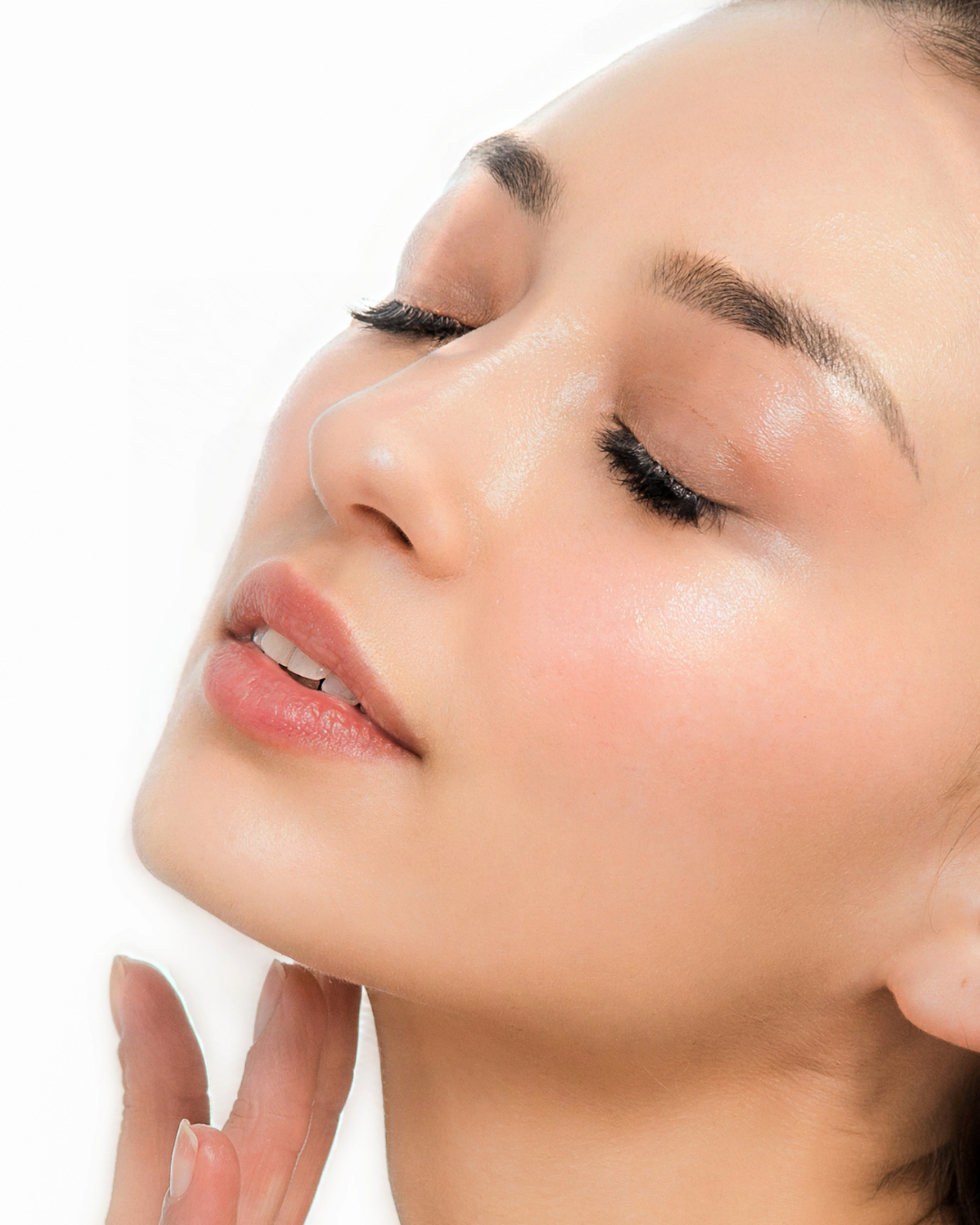 Close-up of a woman with clear skin, closed eyes, light makeup, and her hand gently touching her chin.