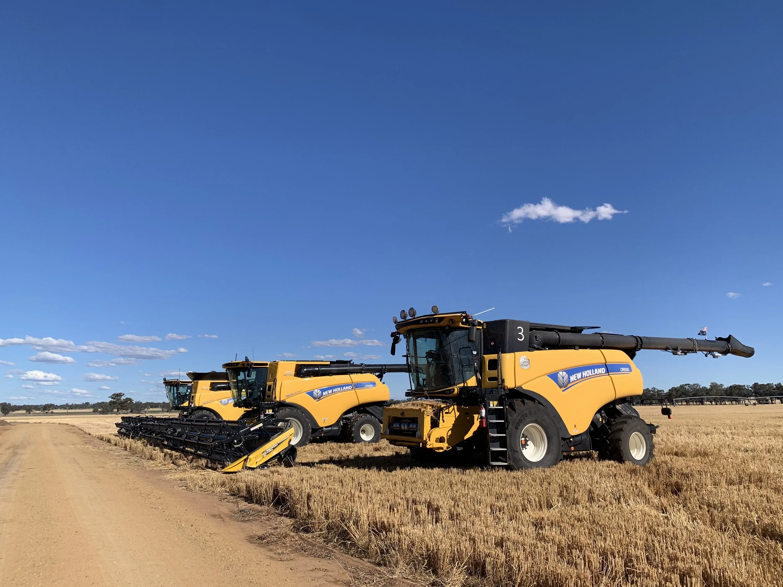 Two large yellow harvesters in a wheat field under a blue sky with clouds.