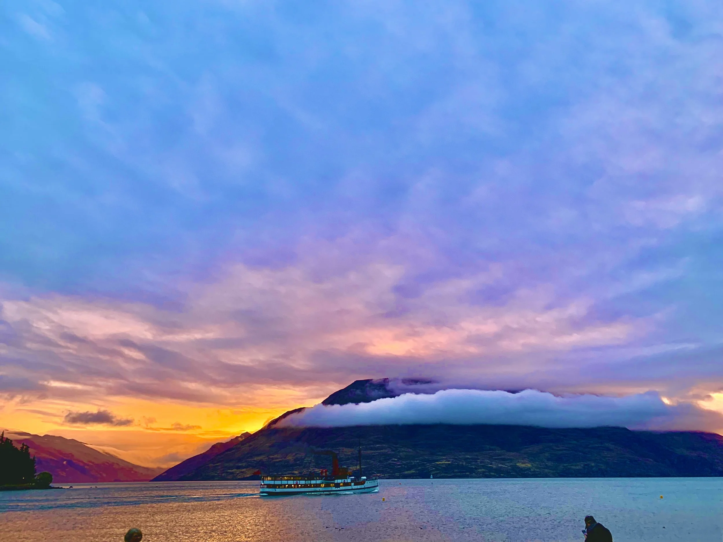 A boat on a lake with mountains and a colorful sky at sunset.