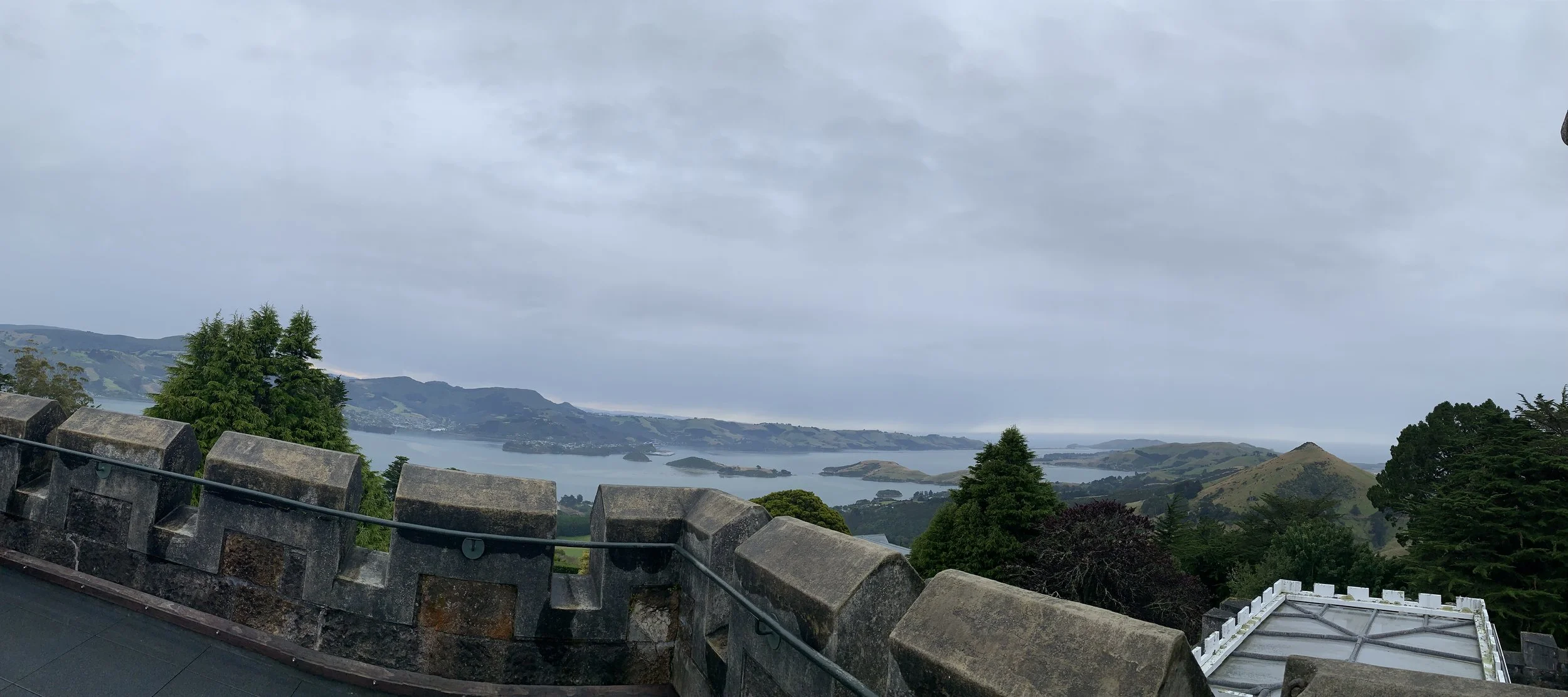 A view from a stone fortress or castle wall overlooking a bay with green hills and islands under an overcast sky.