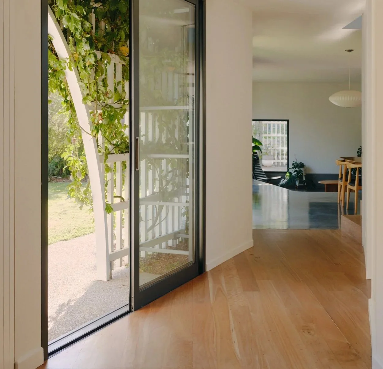 View of a sliding glass door leading to a garden, with a white trellis and green leafy vines outside, and a glimpse of the interior living space in a modern home.