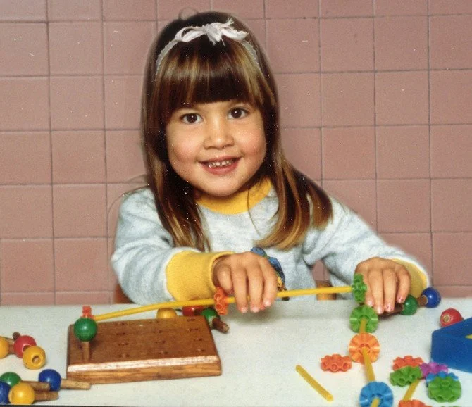 Young girl playing with colorful gear and building toys at a table.