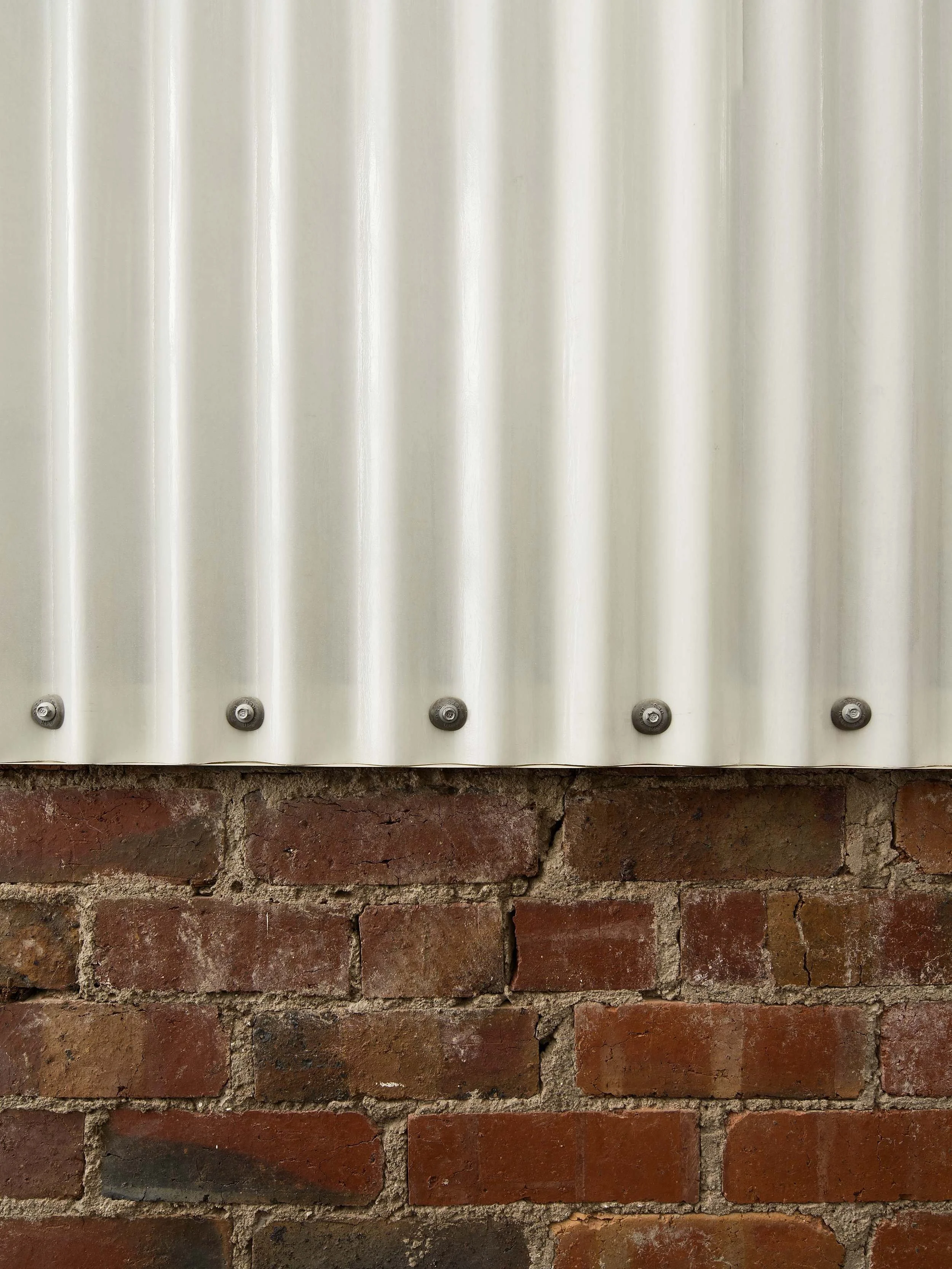 Part of a brick wall with a mounted, corrugated metallic sheet secured with screws.