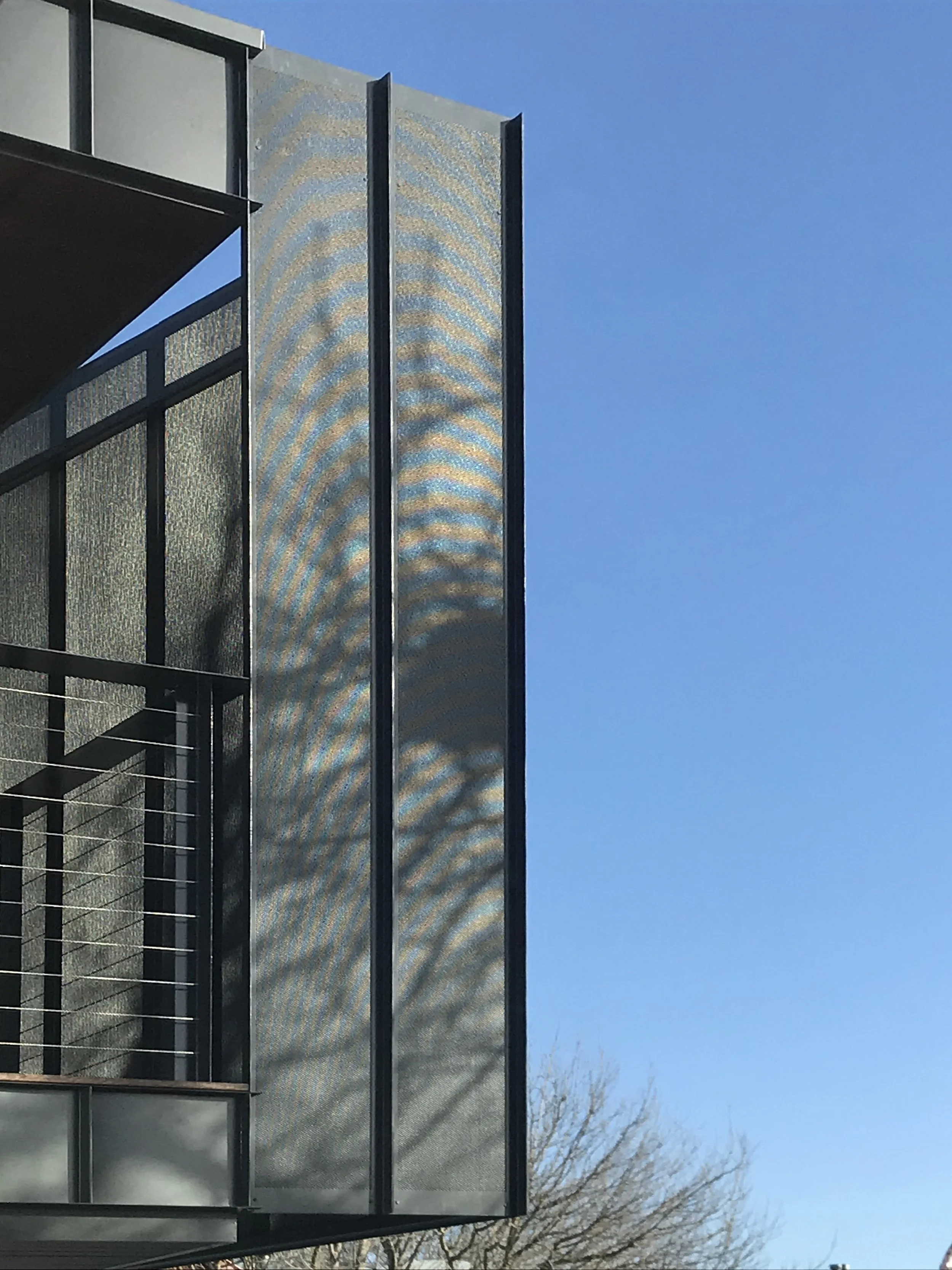 A modern building with a turquoise glass facade and black metal frames under a clear blue sky, with leafless trees in the background.