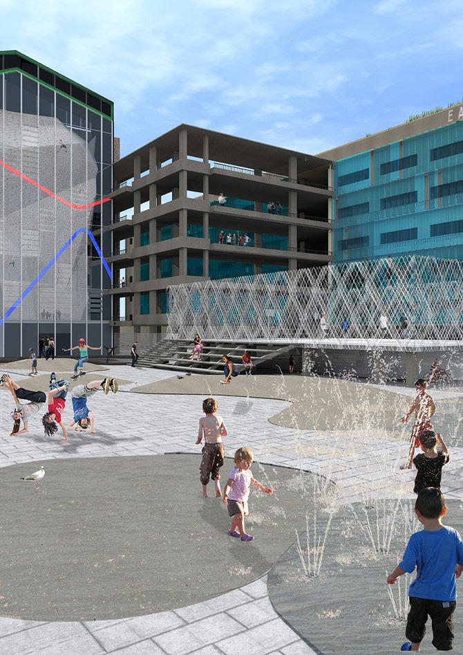 Children playing in a splash pad area with water jets in front of modern buildings with glass windows and structural designs.