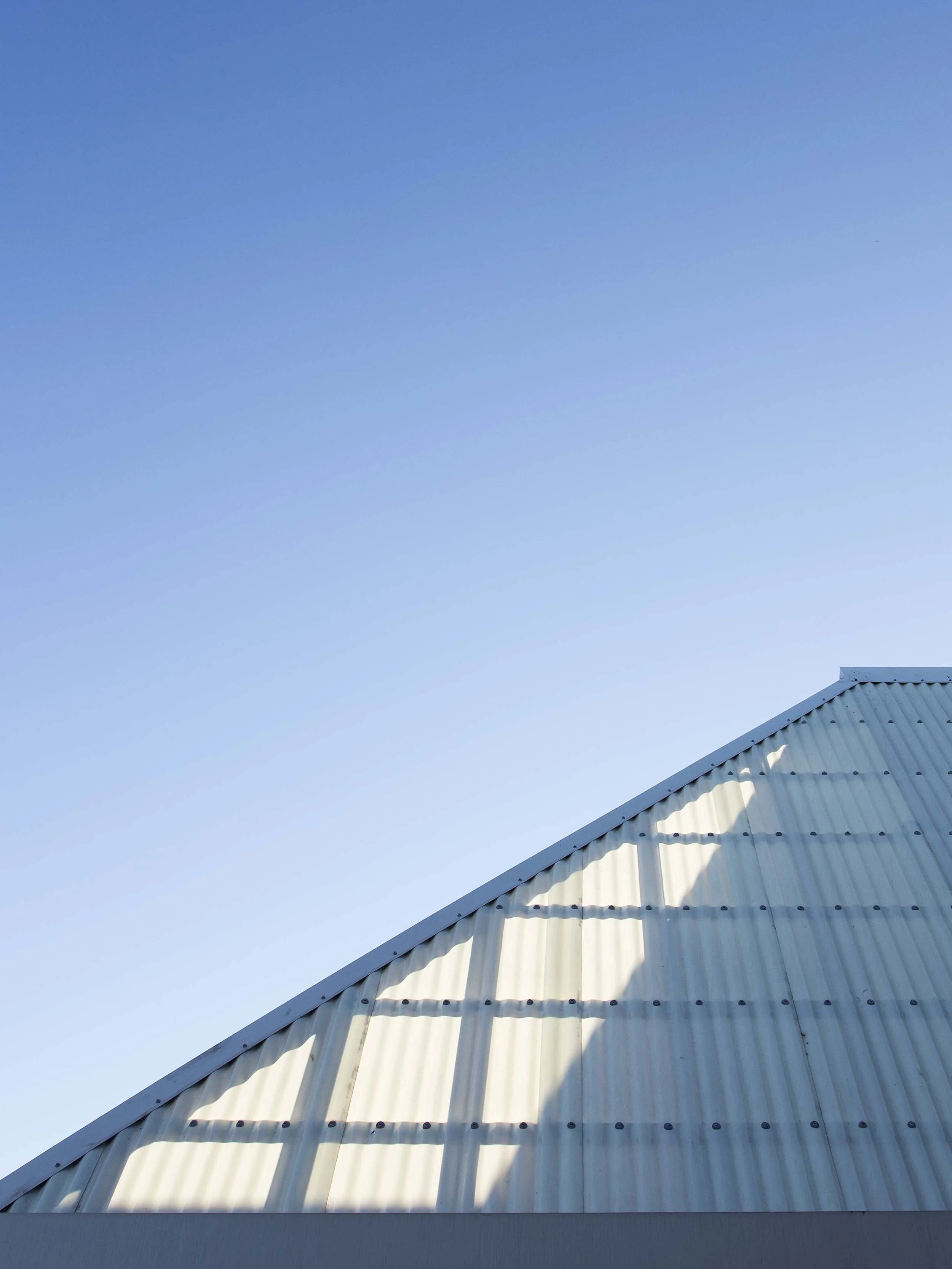 A close-up of a building's metal roof and wall with a clear blue sky in the background.