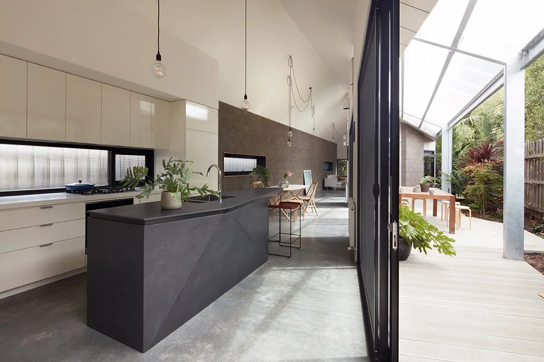 Modern open-concept kitchen with black island, white cabinets, and outdoor dining area with trees visible outside