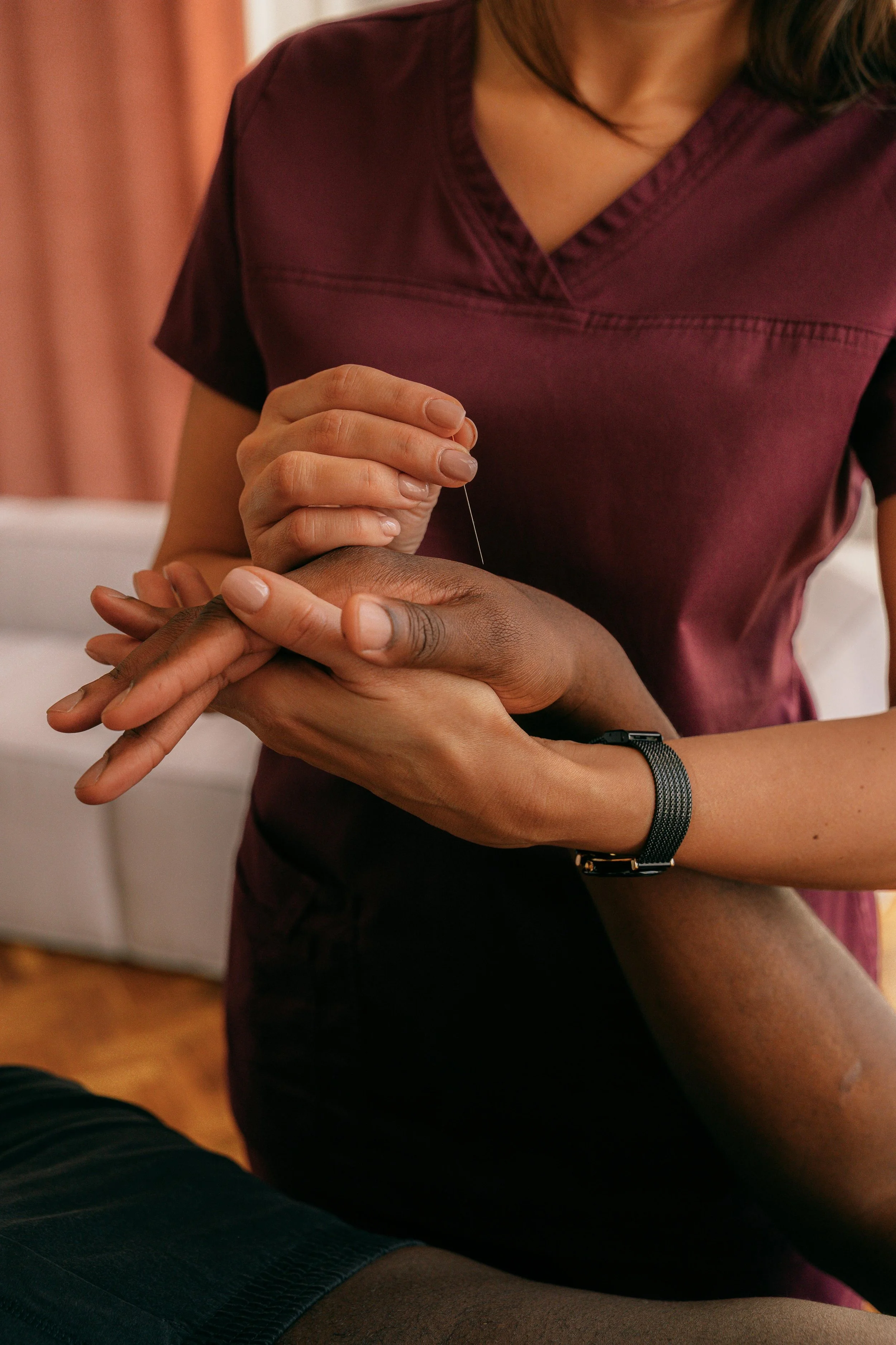 A healthcare professional is performing acupuncture on a patient's hand, inserting a thin needle into specific points.