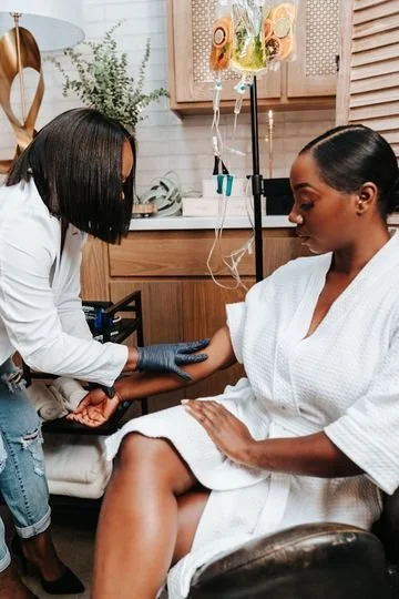 A woman receiving an IV infusion from a healthcare professional in a clinic setting.