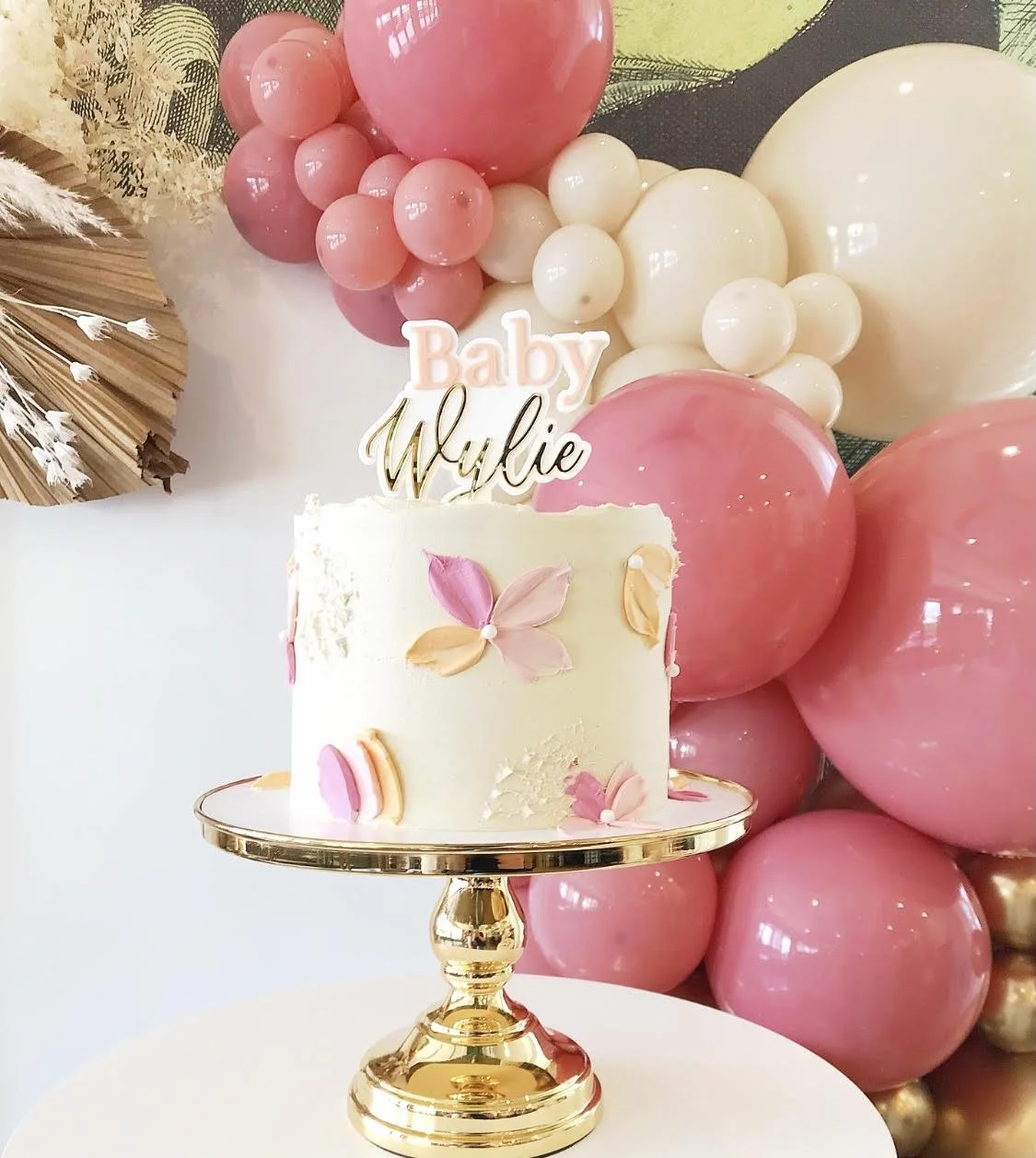 A baby shower cake on a gold cake stand and cake plinth