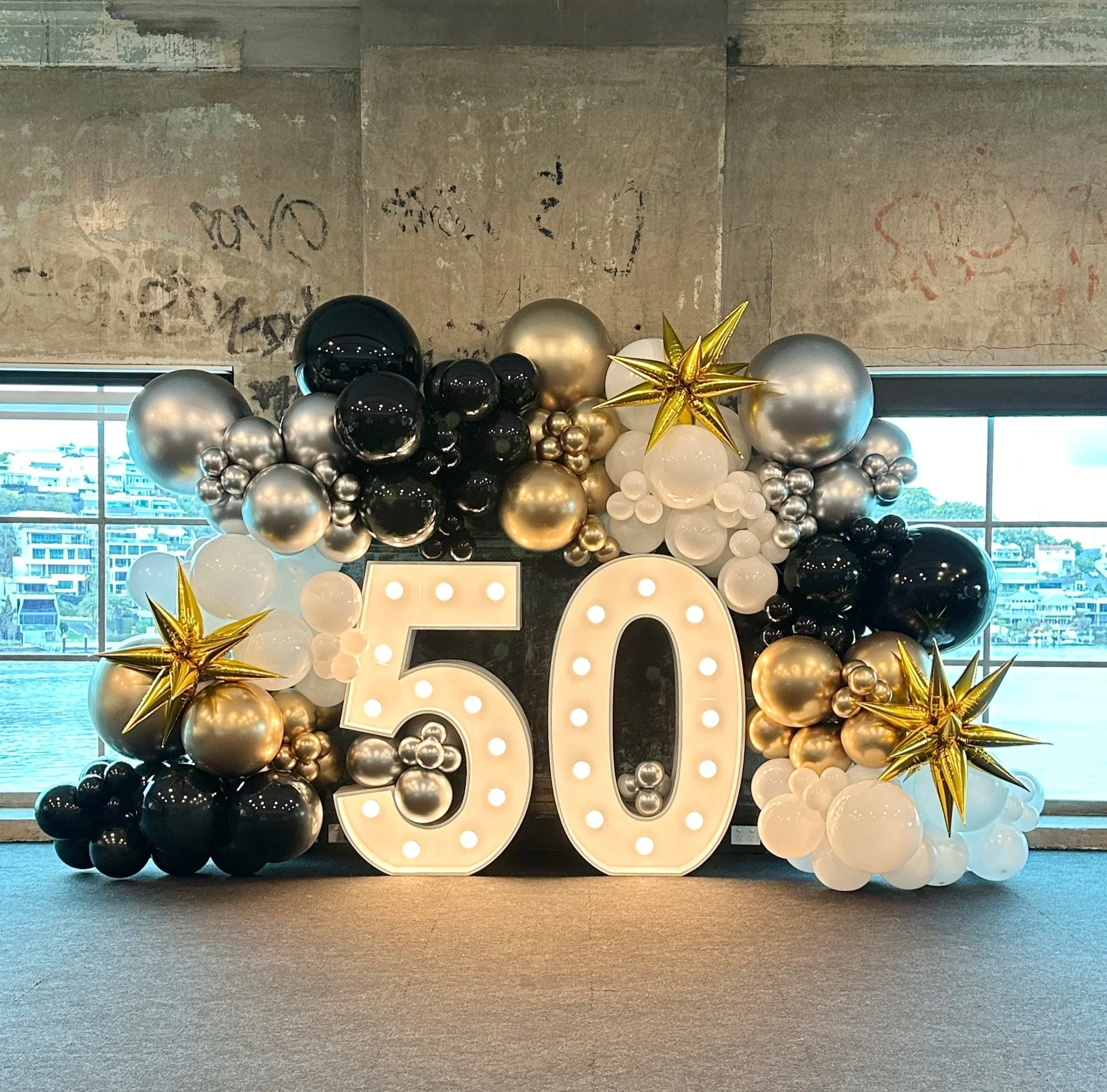 Decorative balloon arrangement celebrating 50th anniversary with large illuminated number 50 surrounded by a balloon wall