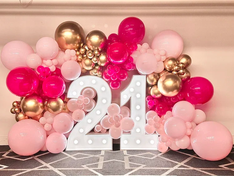 Decorative balloon arrangement with pink, gold, and white balloons surrounding a large illuminated number 24 for a celebration.