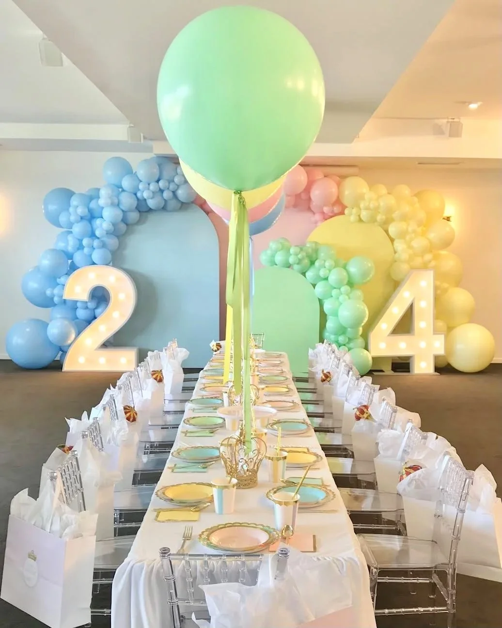Decorated birthday party table with pastel balloons, large illuminated number 2 and 4, and a colorful balloon arch in the background