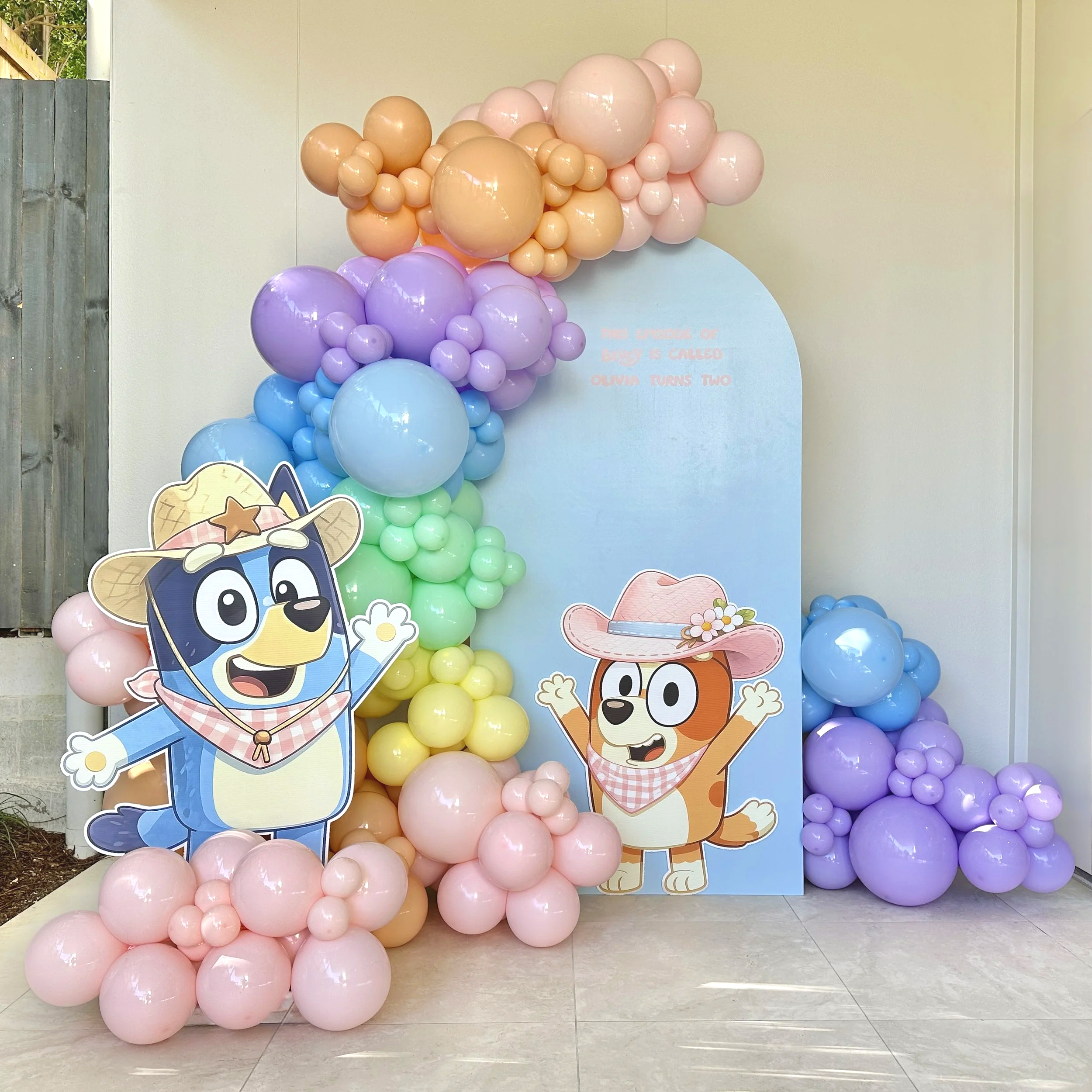 Decorative setup with pastel-colored balloons arranged in clusters, featuring cartoon images of a dog and a bear on a light blue background, indicating a child's birthday celebration.