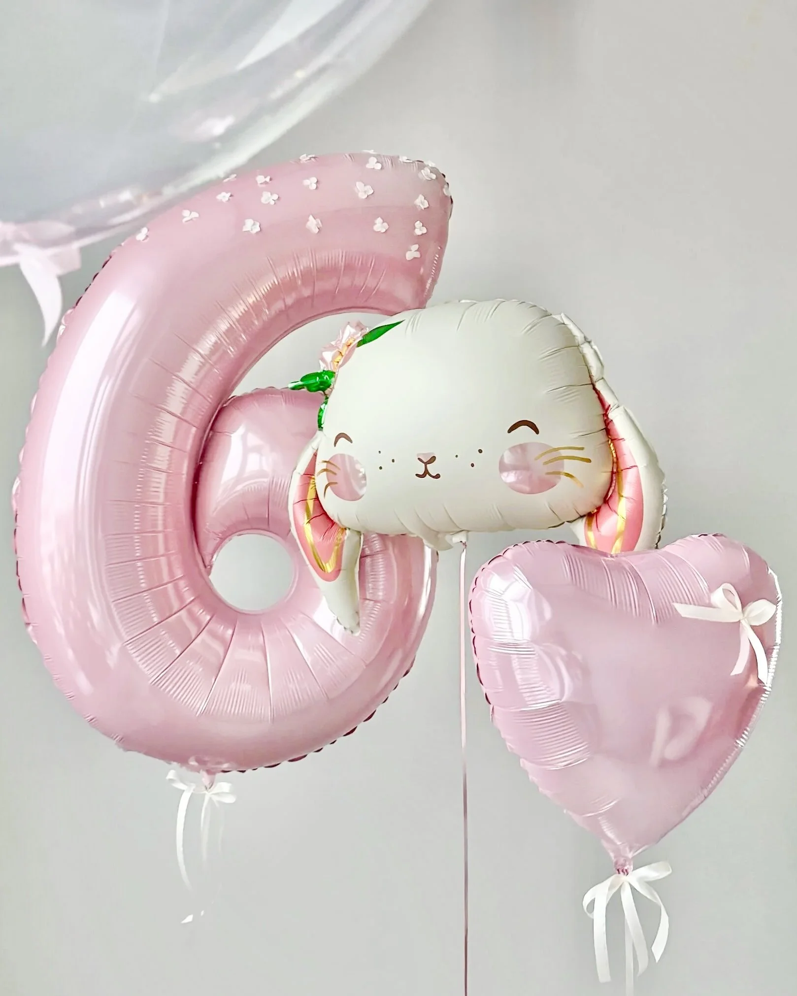 Collection of pink and white foil balloons, including a bear-shaped balloon, against a plain background.